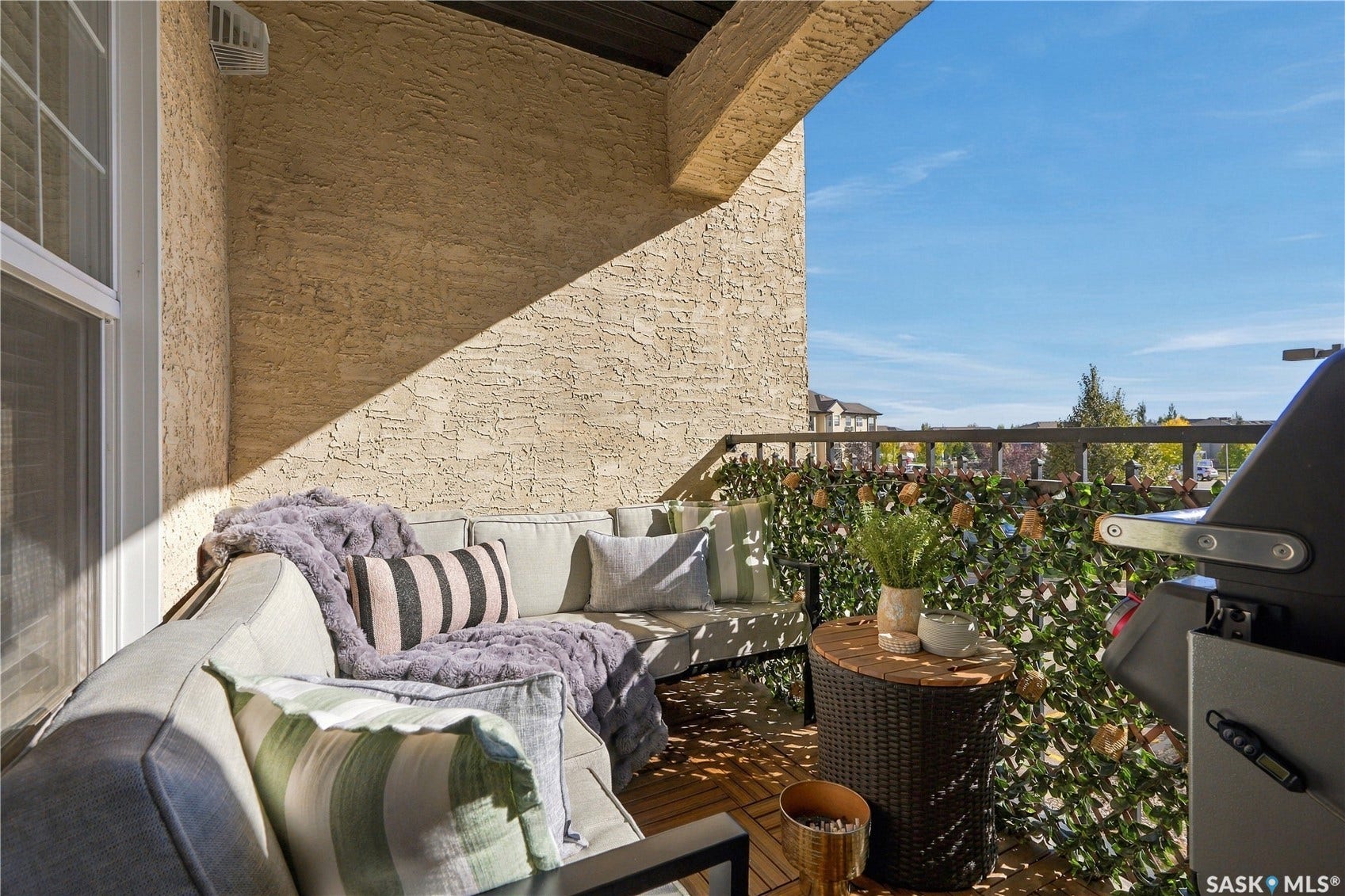 Balcony with textured exterior wall, slatted wood flooring, dark-stained railing, and partial overhead coverage