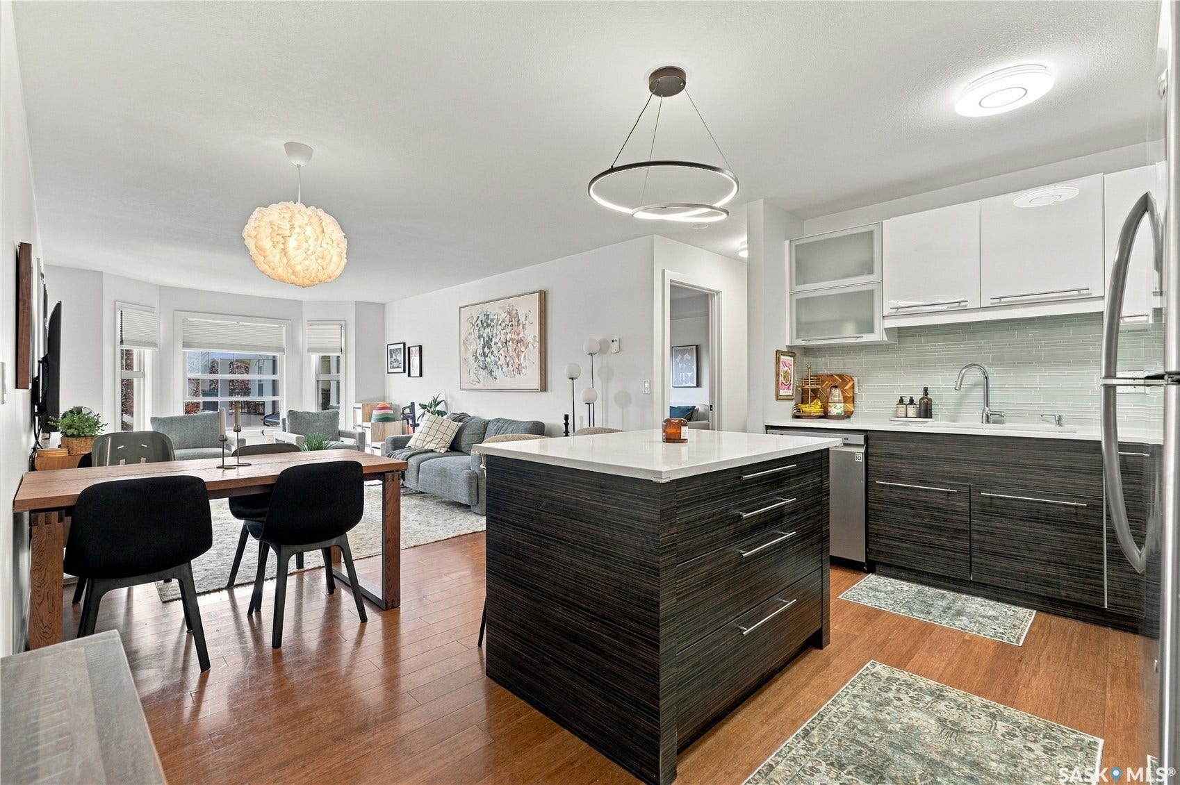 Open-concept living space featuring wood-finish flooring, a kitchen island with a light-toned countertop, white upper cabinetry, and a bay window