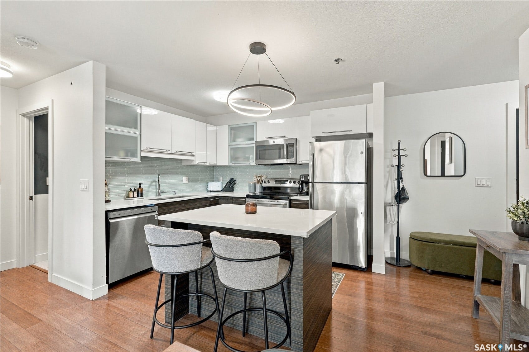 Contemporary kitchen featuring stainless steel appliances, white cabinetry, a central island with countertop seating, wood-finish flooring, and a modern pendant light fixture