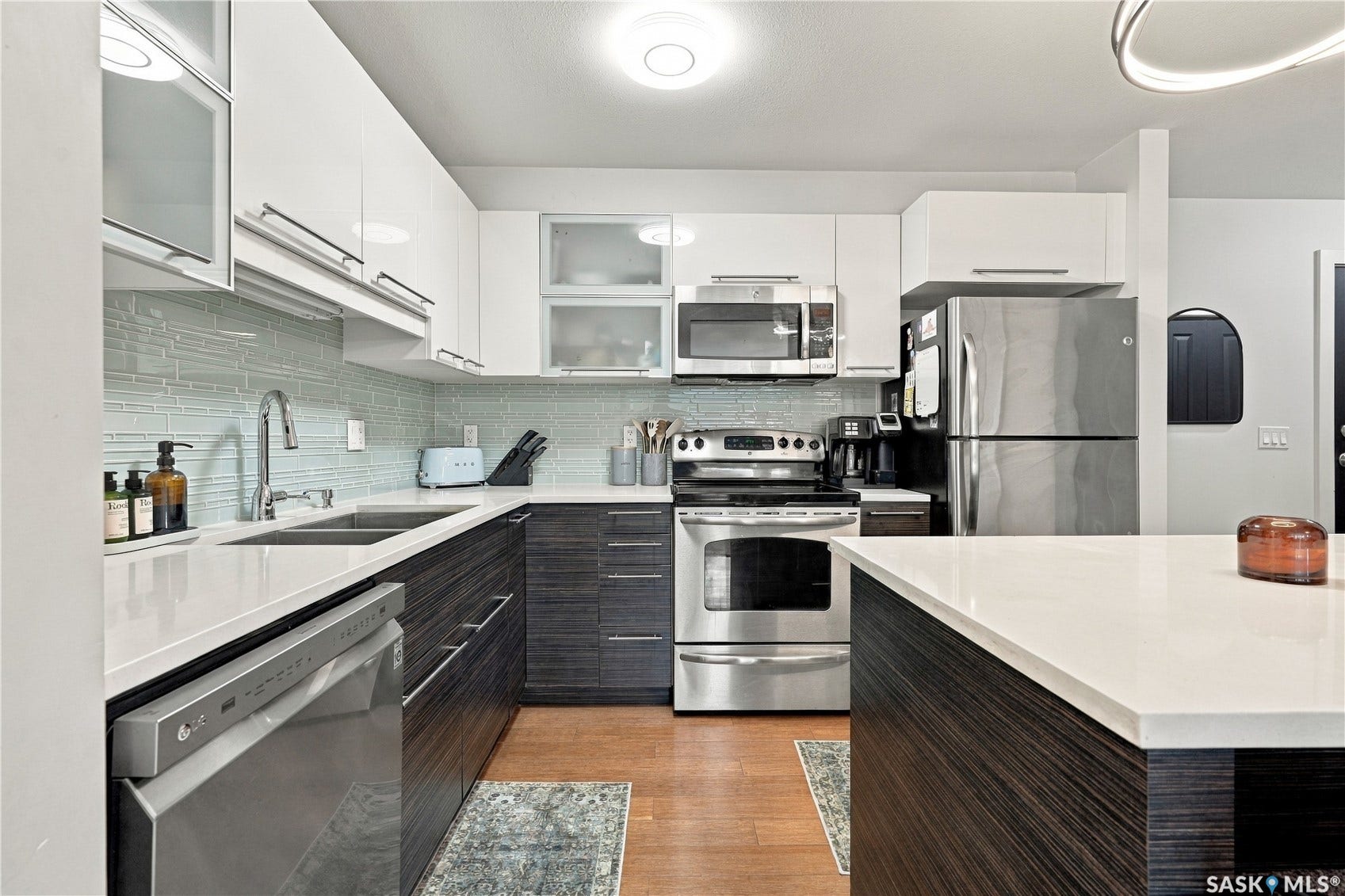 Modern kitchen featuring white upper cabinetry, dark wood-finish lower cabinetry, light countertop, stainless steel appliances, and a tile backsplash