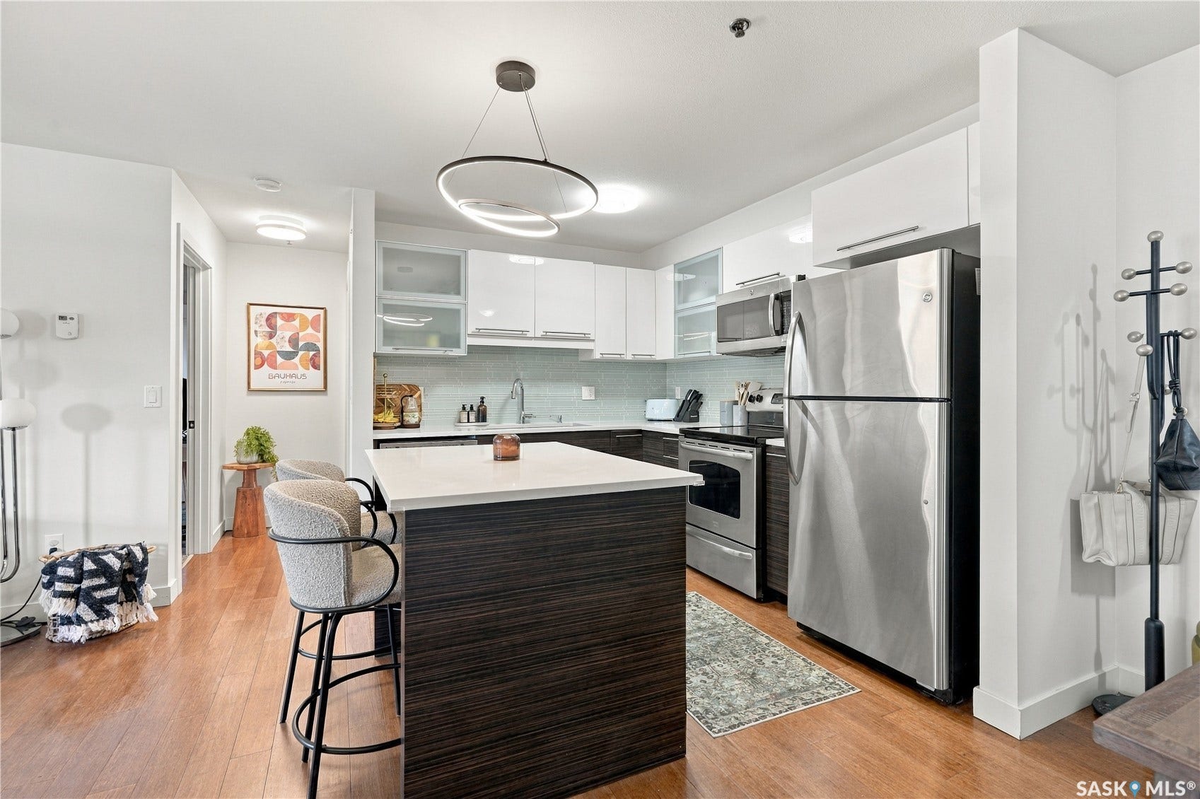 Open-concept kitchen featuring an island with seating, stainless steel appliances, white flat-panel cabinetry, a light-toned backsplash, and wood-finish flooring