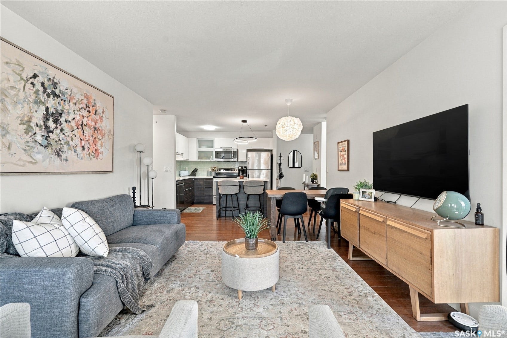 Wood-finish flooring throughout, with a recessed kitchen featuring stainless steel appliances, a breakfast bar, and pendant lighting