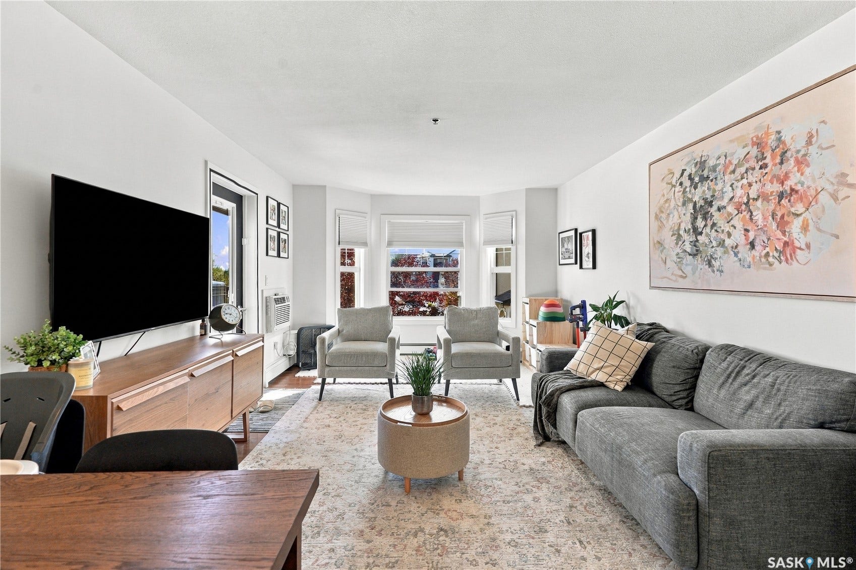Hardwood flooring, bay window, white walls, built-in air conditioning unit, and a built-in shelving unit