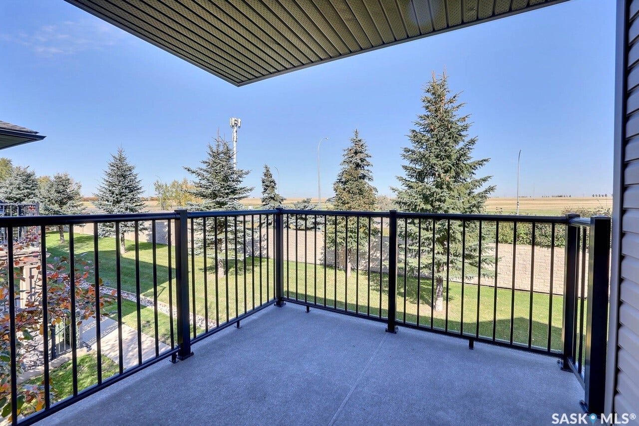 Outdoor balcony with black metal railing, concrete flooring, and an overhead soffit