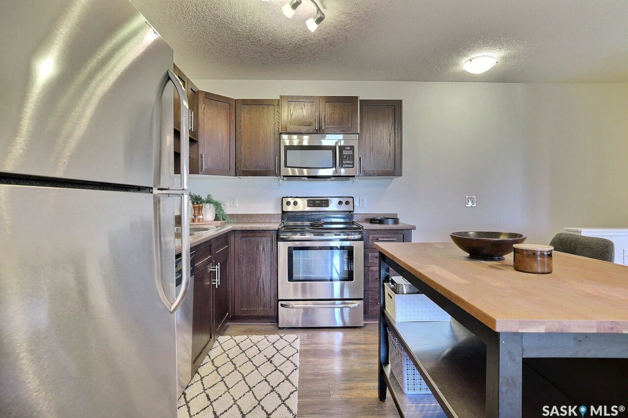 Stainless steel appliance suite, dark wood-finish cabinetry, light-toned countertops, wood-finish flooring, and a butcher block island