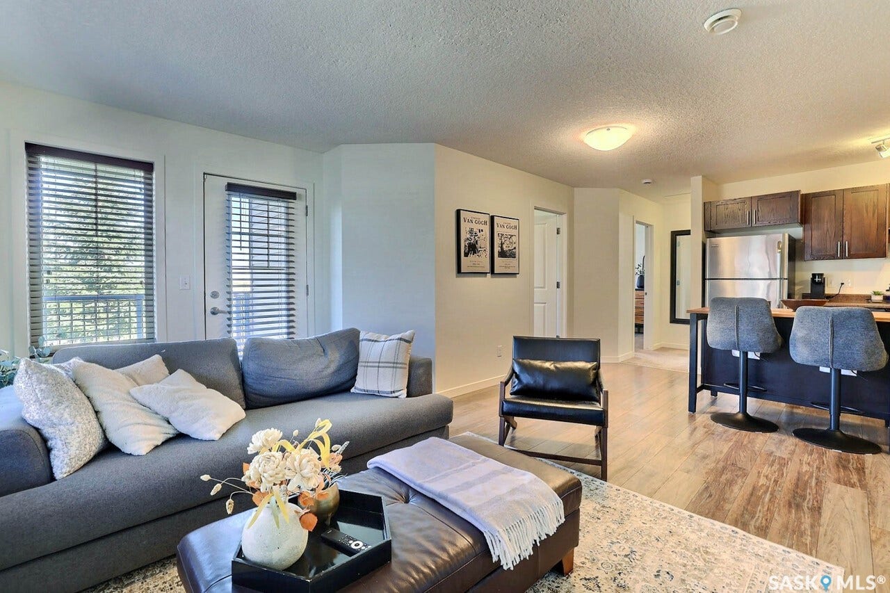 Open-concept living space with wood-finish flooring, a stainless steel refrigerator, and dark wood kitchen cabinetry