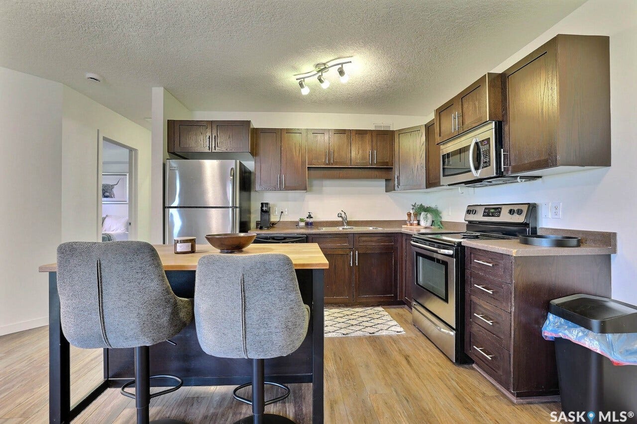 Kitchen featuring wood-finish flooring, dark wood cabinetry, stainless steel appliances, and track lighting