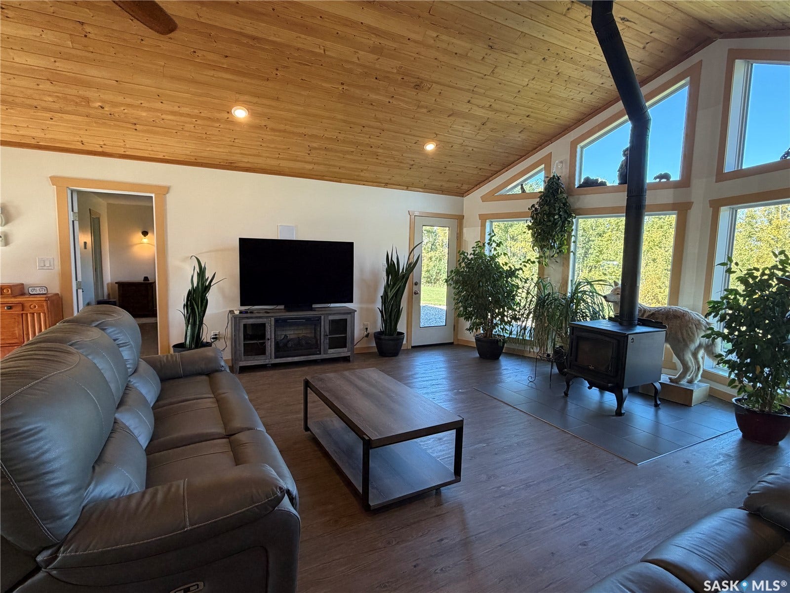 Vaulted wood-paneled ceiling, wood-finish flooring, floor-to-ceiling windows, built-in wood-burning stove, and a ceiling fan