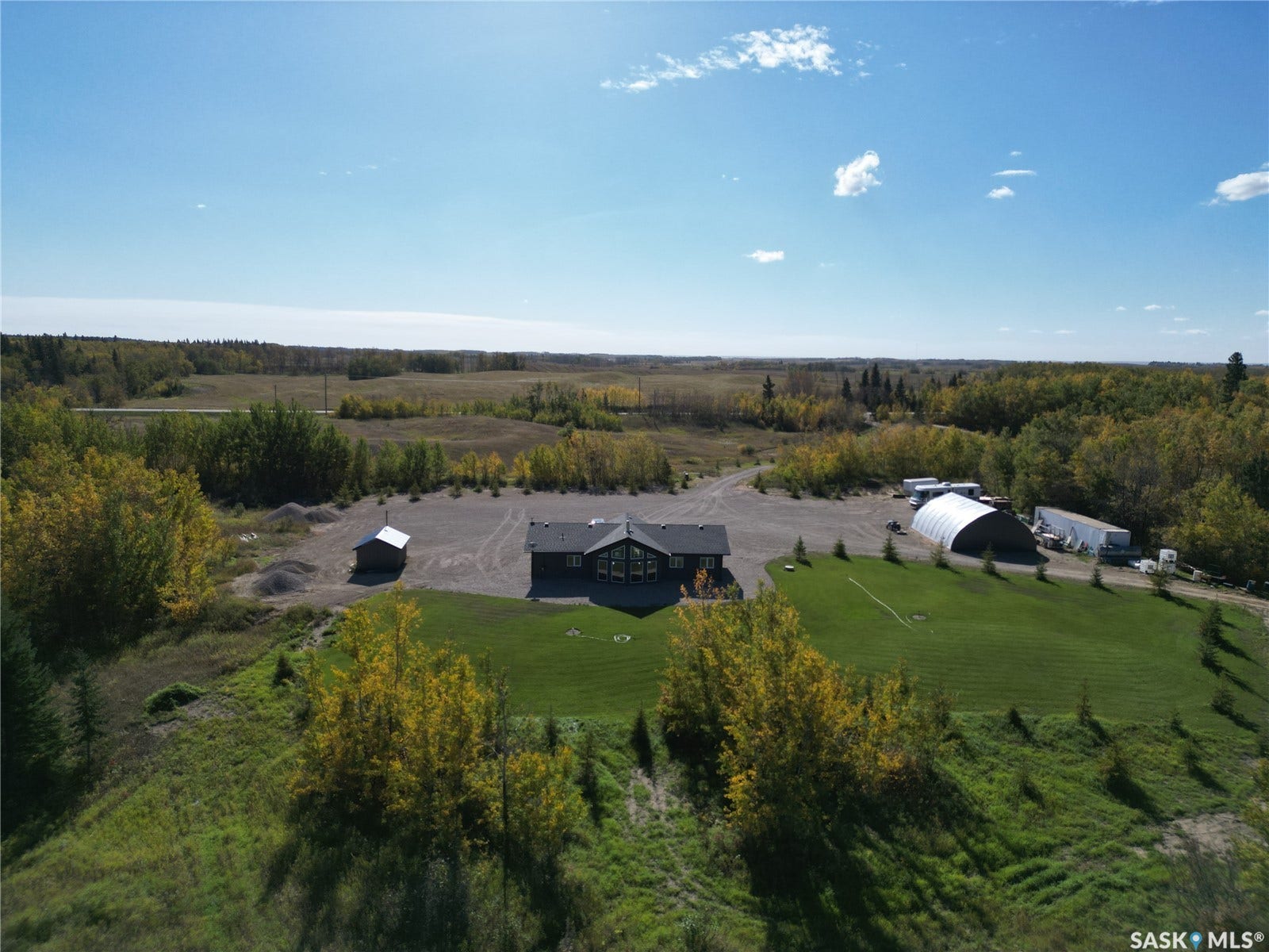Expansive green lawn with surrounding natural landscape, gravel driveway, and a detached shed