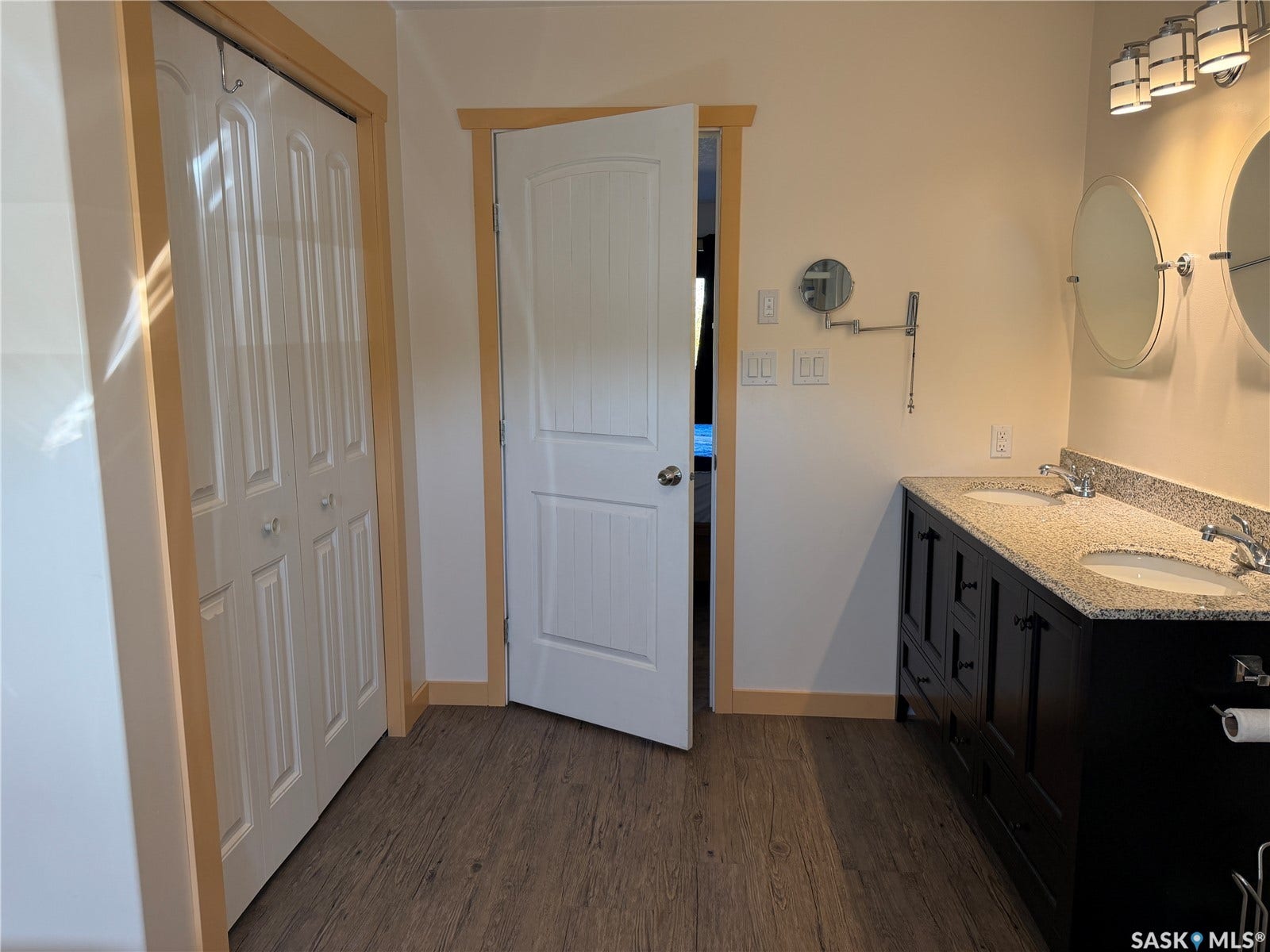 Double vanity with undermount sinks, granite countertop, and wood-finish flooring