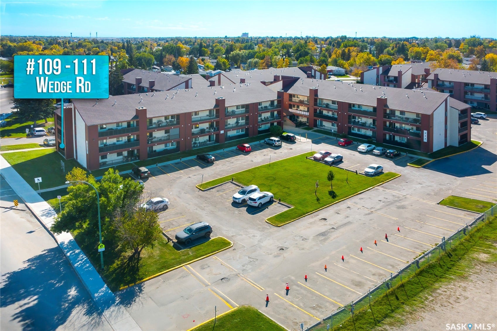 Multi-story building with brick exterior, multiple balconies, and an expansive parking area