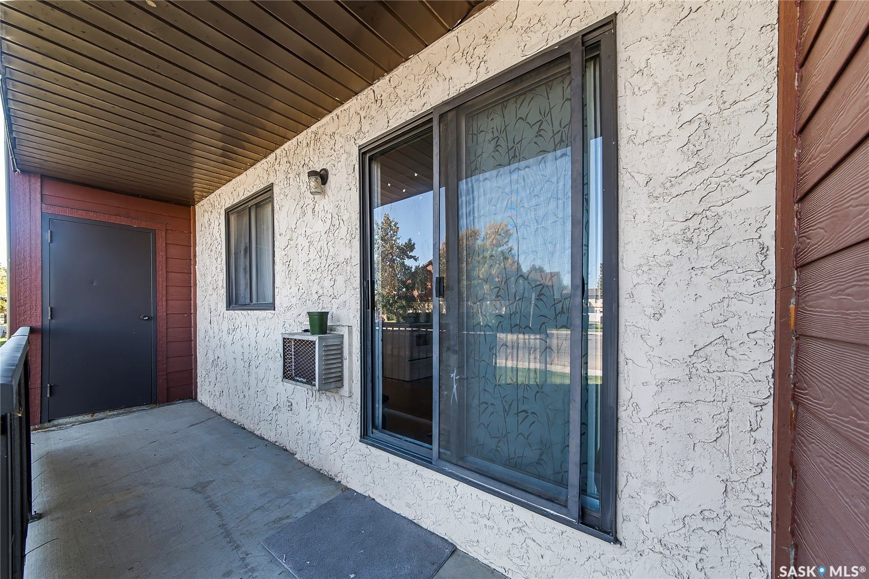 Concrete patio with stucco exterior, a sliding glass door, and an exterior light fixture