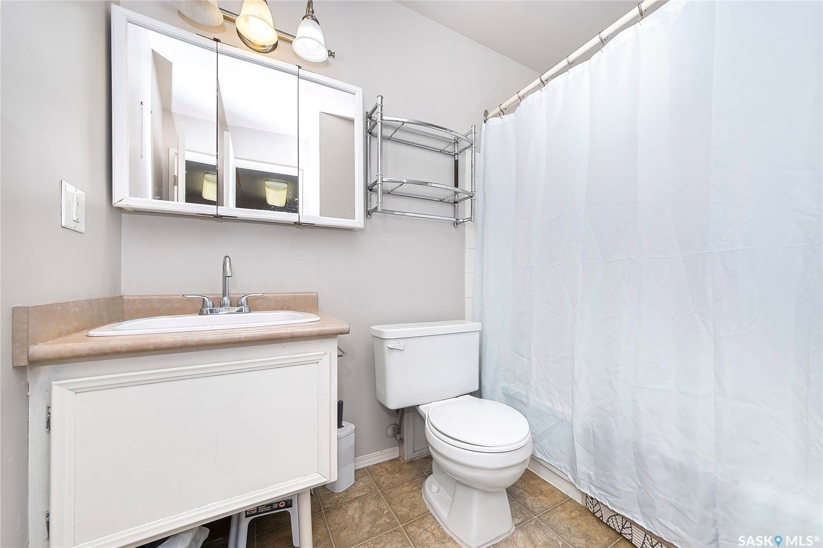 Bathroom featuring a white vanity with a tan countertop, a surface-mount sink, a mirrored medicine cabinet, and a shower area