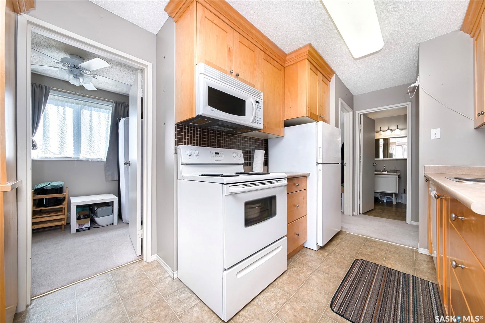 Galley kitchen featuring wood cabinetry, tile flooring, and white appliances