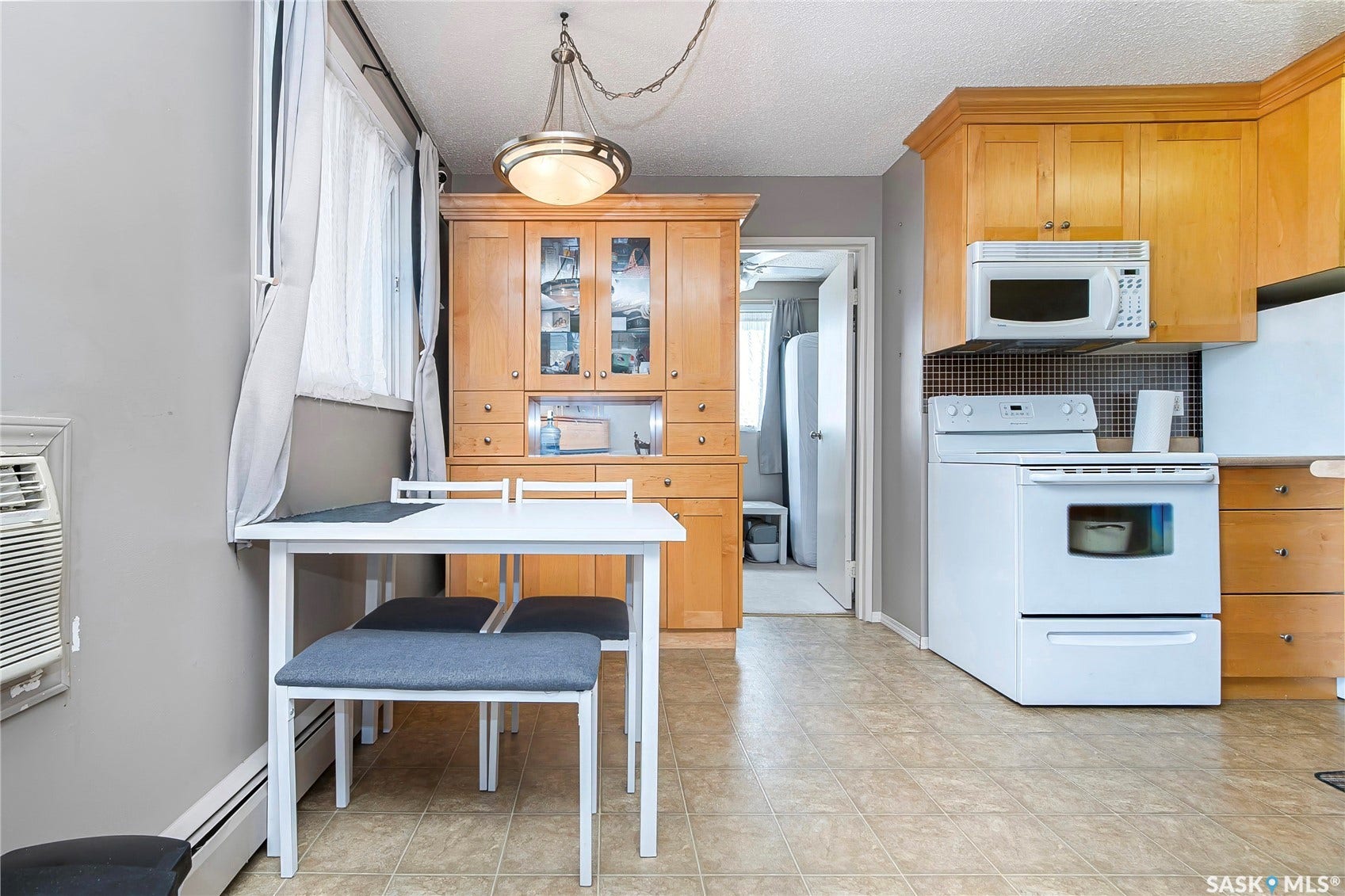 Light wood-finish cabinetry, tile-pattern flooring, integrated overhead microwave, built-in wall unit, and a window with natural light