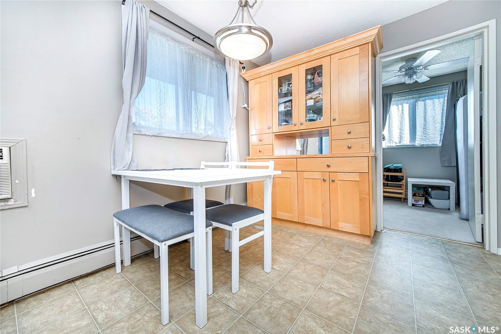 Built-in wood cabinetry with glass-front upper doors, tiled flooring, window with sheer and fabric curtains, and a ceiling light fixture