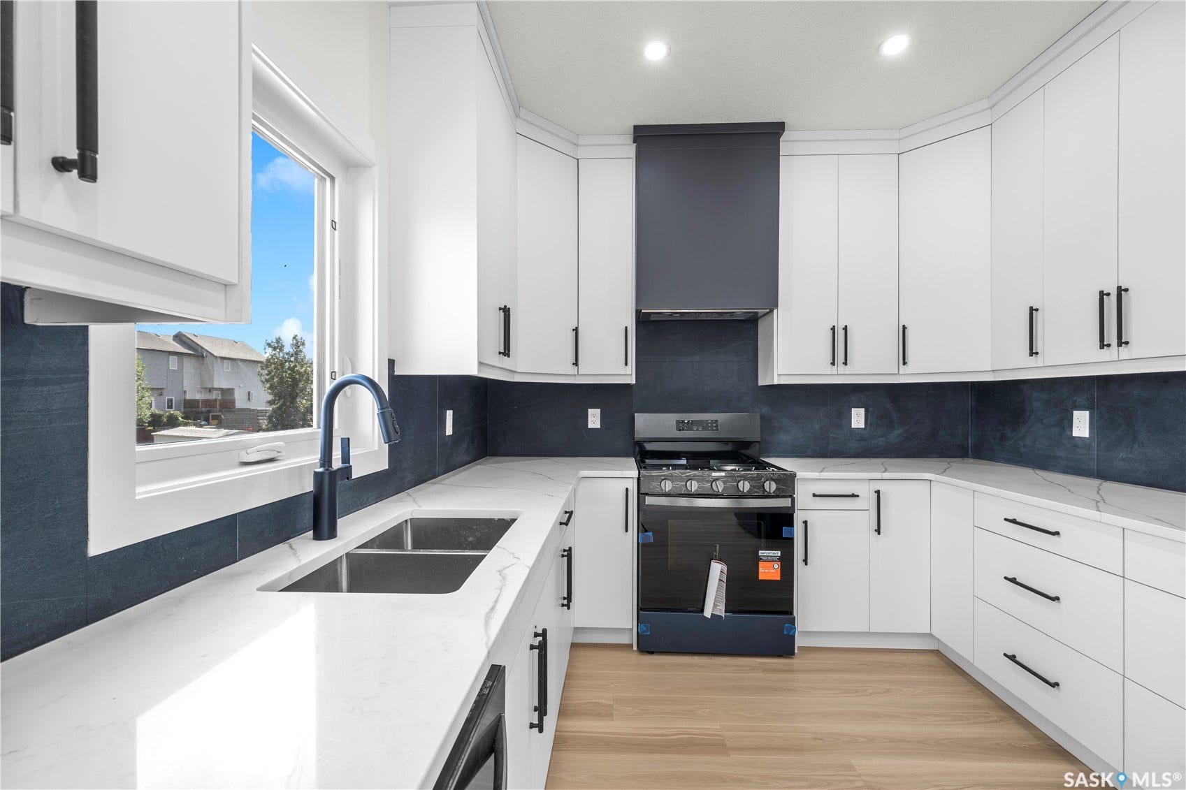 White cabinetry with matte black hardware, stone countertops, dark tile backsplash, stainless steel double basin sink with black faucet, and wood-finish flooring