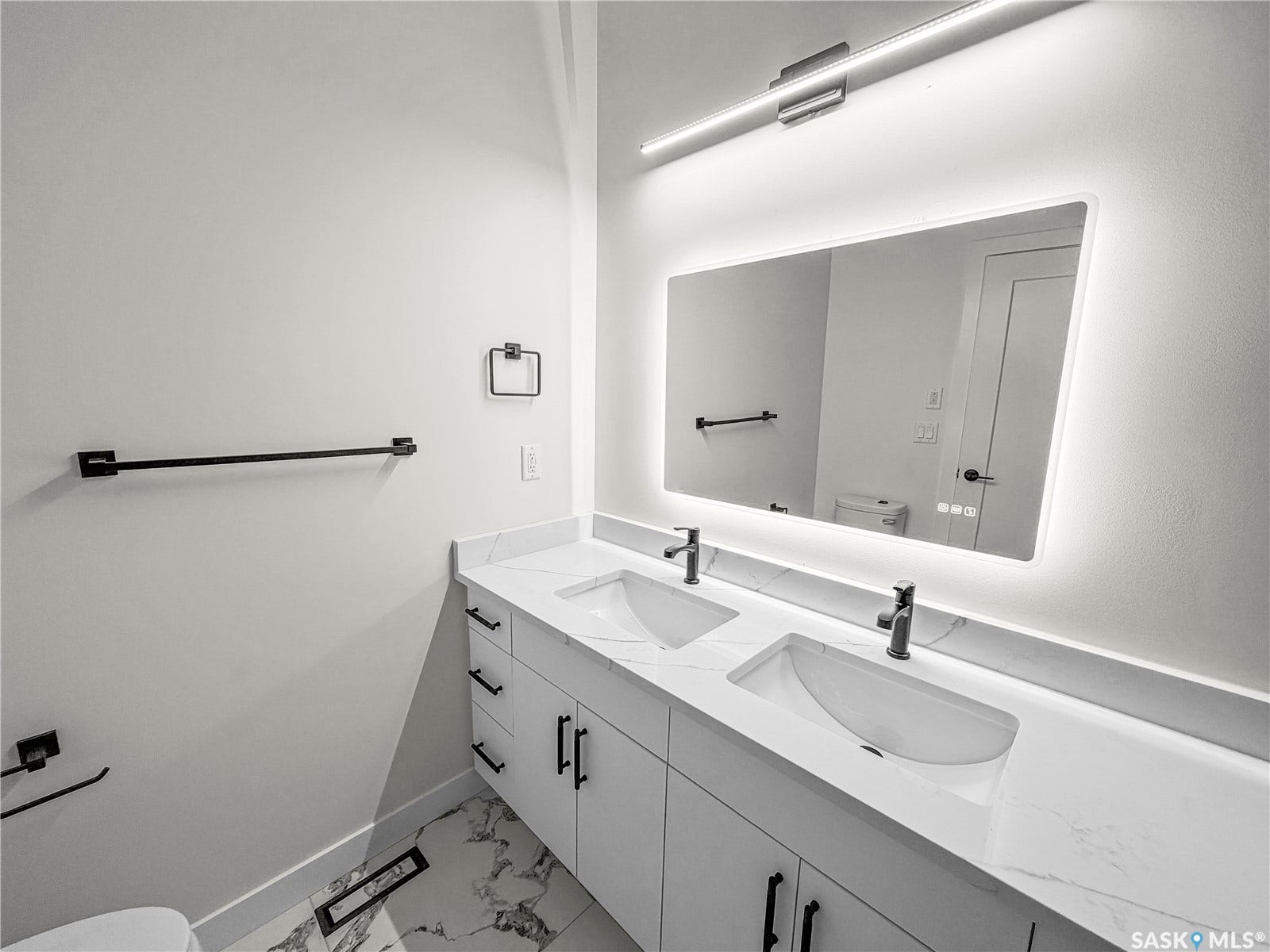 Dual undermount sinks with matte black faucets, quartz countertops, white cabinetry, and an illuminated vanity mirror