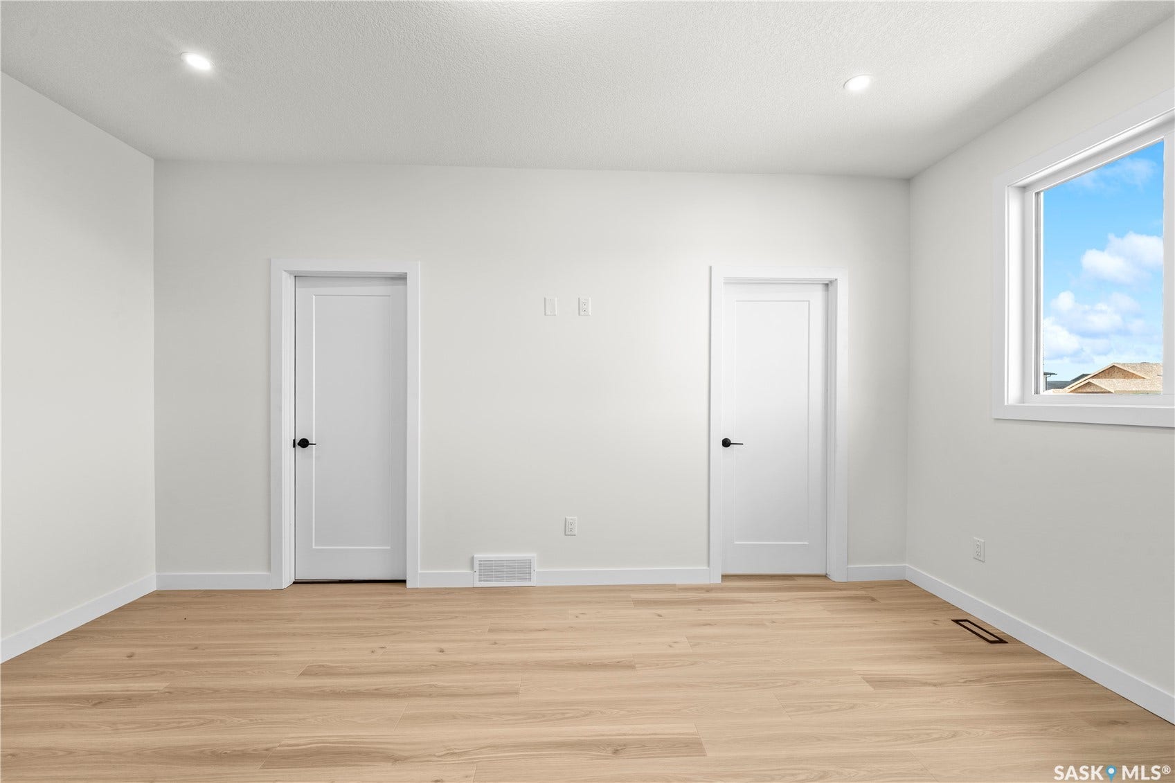 Recessed ceiling lighting, light wood-finish flooring, white trim, white interior doors with black hardware, and a window with white framing