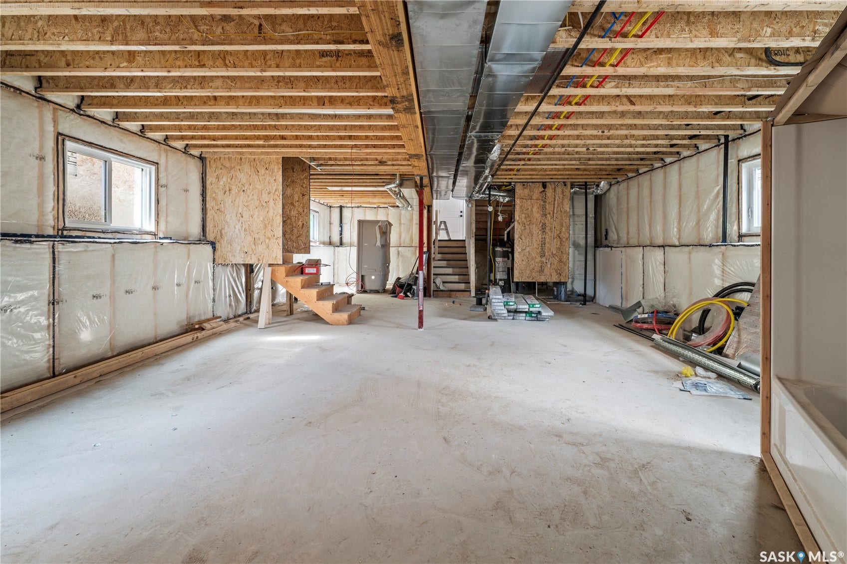Spacious unfinished basement featuring exposed ceiling joists, concrete flooring, and multiple windows