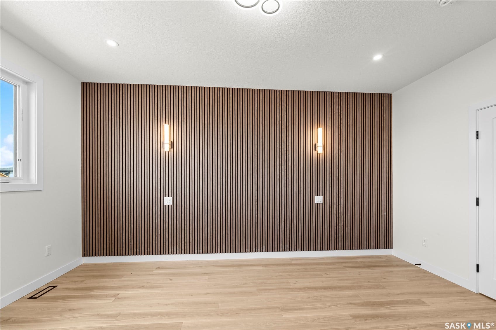 Accent wall featuring vertical wood paneling, two wall sconces, recessed ceiling lighting, and wood-finish flooring