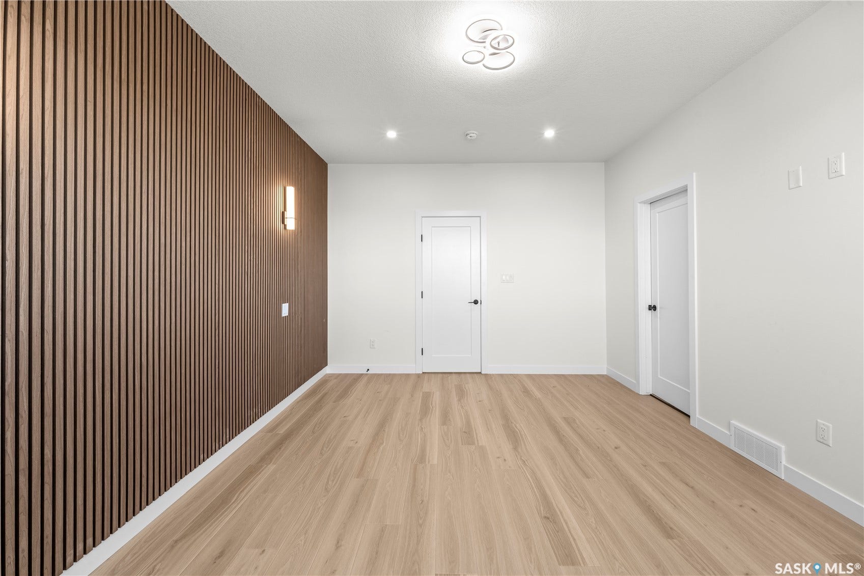 Wood-slat accent wall with integrated sconce, recessed lighting, contemporary ceiling fixture, and light wood-finish flooring