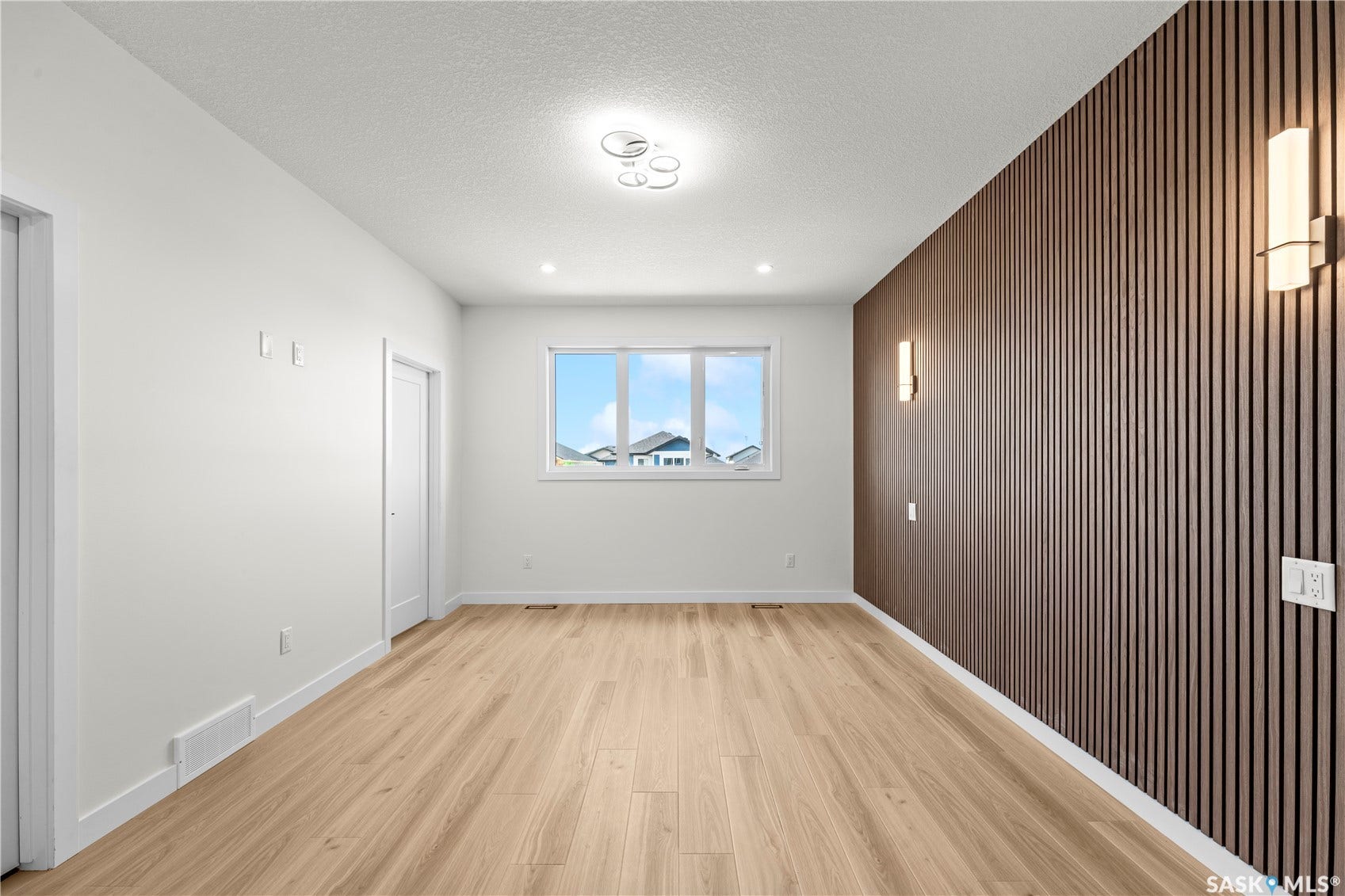 Wood-finish flooring with a textured accent wall, featuring built-in sconce lighting and a contemporary ceiling fixture
