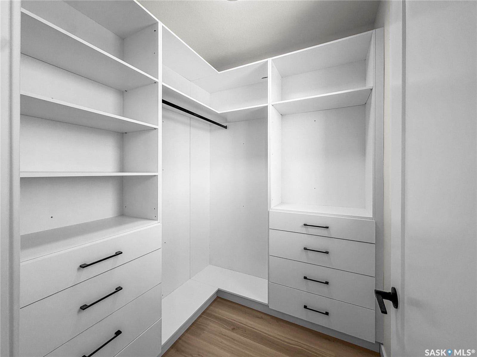 Built-in white shelving system with hanging rod, integrated drawers with black hardware, and wood-finish flooring