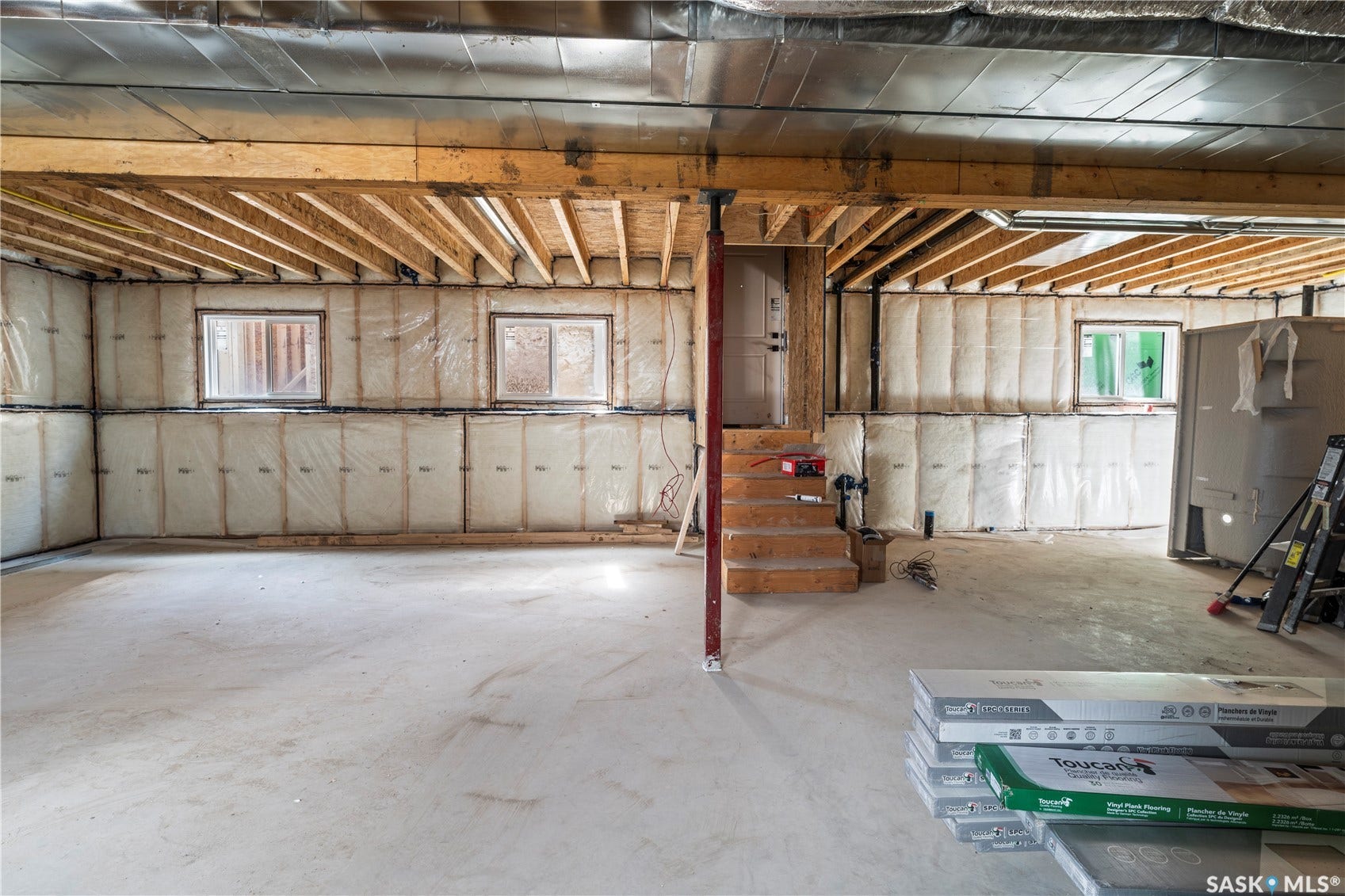 Unfinished basement with concrete flooring and exposed wood ceiling joists, featuring multiple windows and a wood-finished staircase