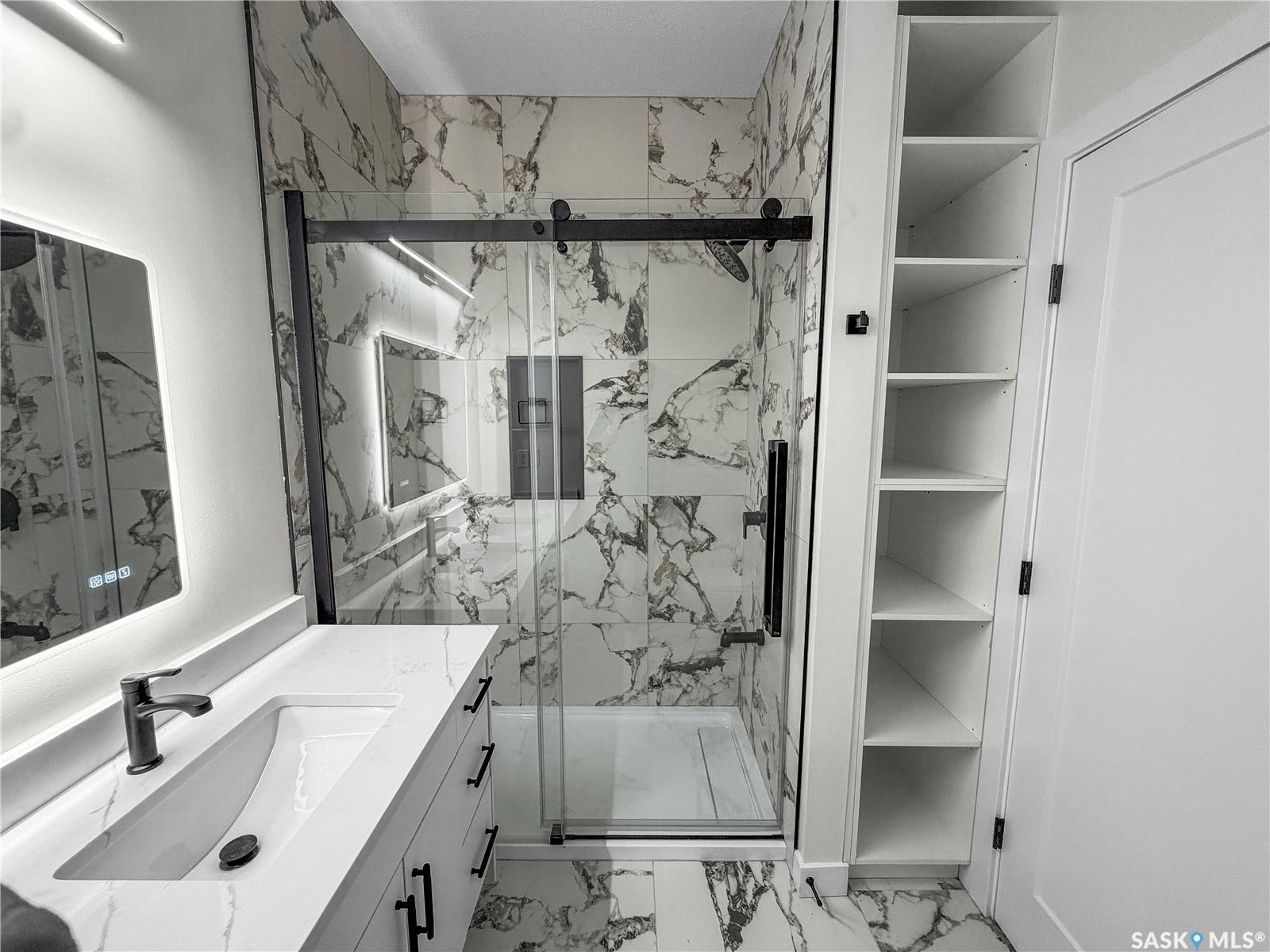 Sleek bathroom featuring a vanity with an integrated sink and matte black faucet, a walk-in shower with a glass enclosure and black hardware, and an illuminated mirrored medicine cabinet