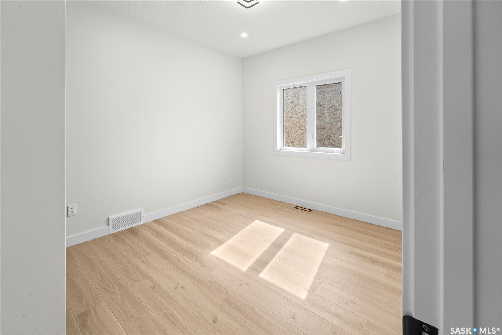 Light wood-finish flooring, recessed ceiling lighting, a white framed window, and white painted walls