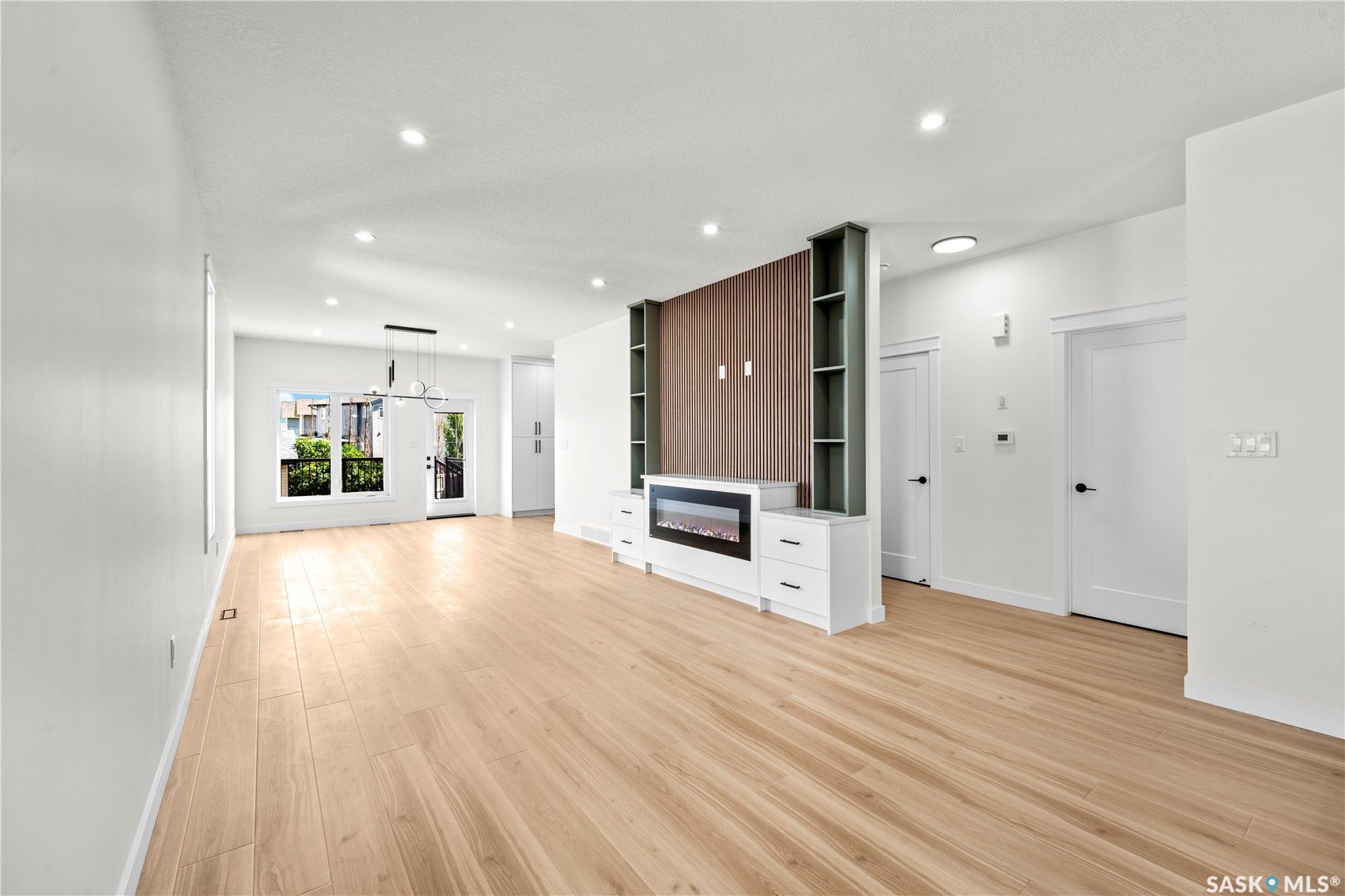 Spacious open-concept interior featuring light wood-finish flooring, recessed lighting, and a built-in media console with an electric fireplace