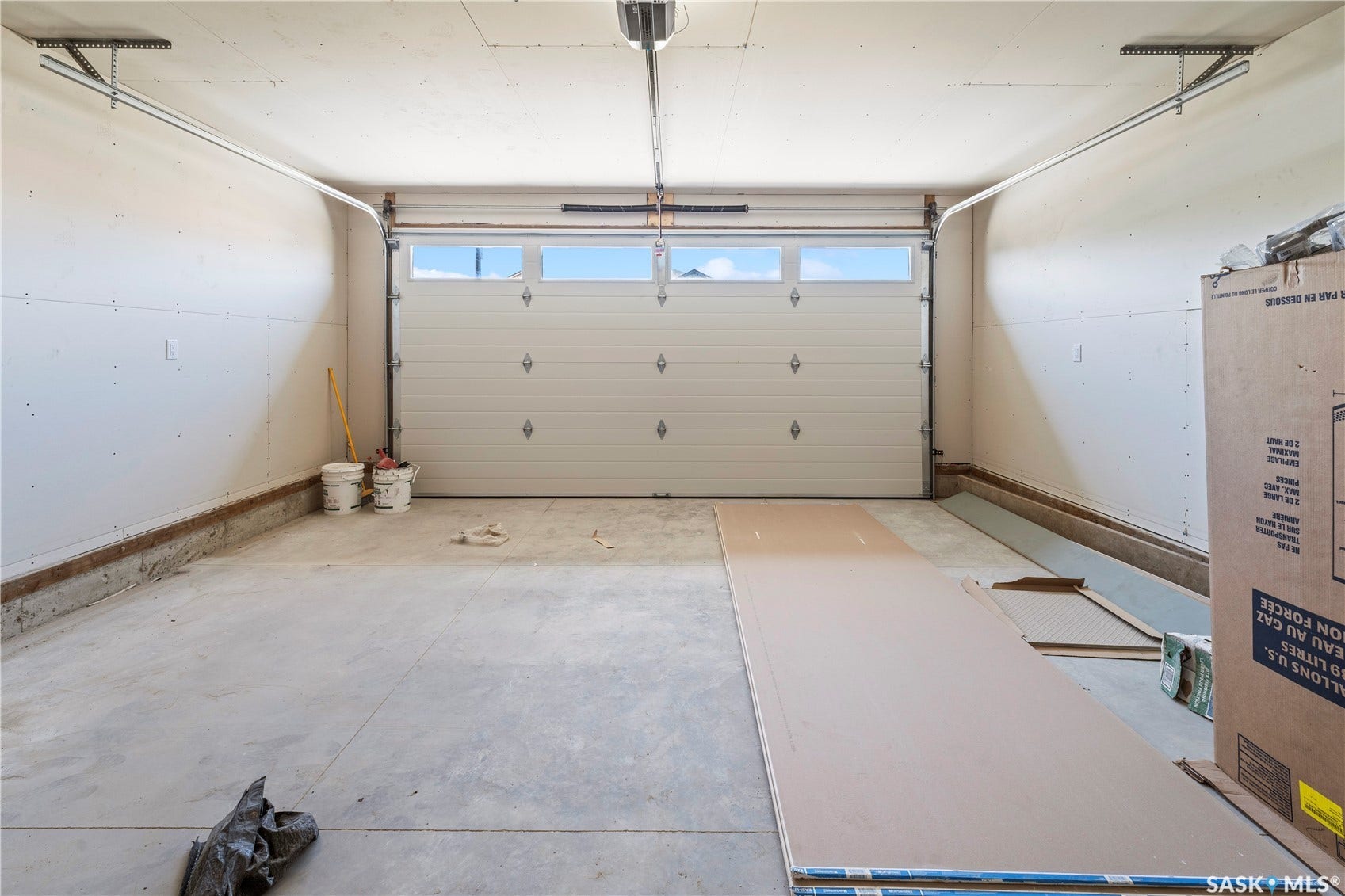 White paneled garage door with upper window inserts, concrete flooring, and unfinished walls