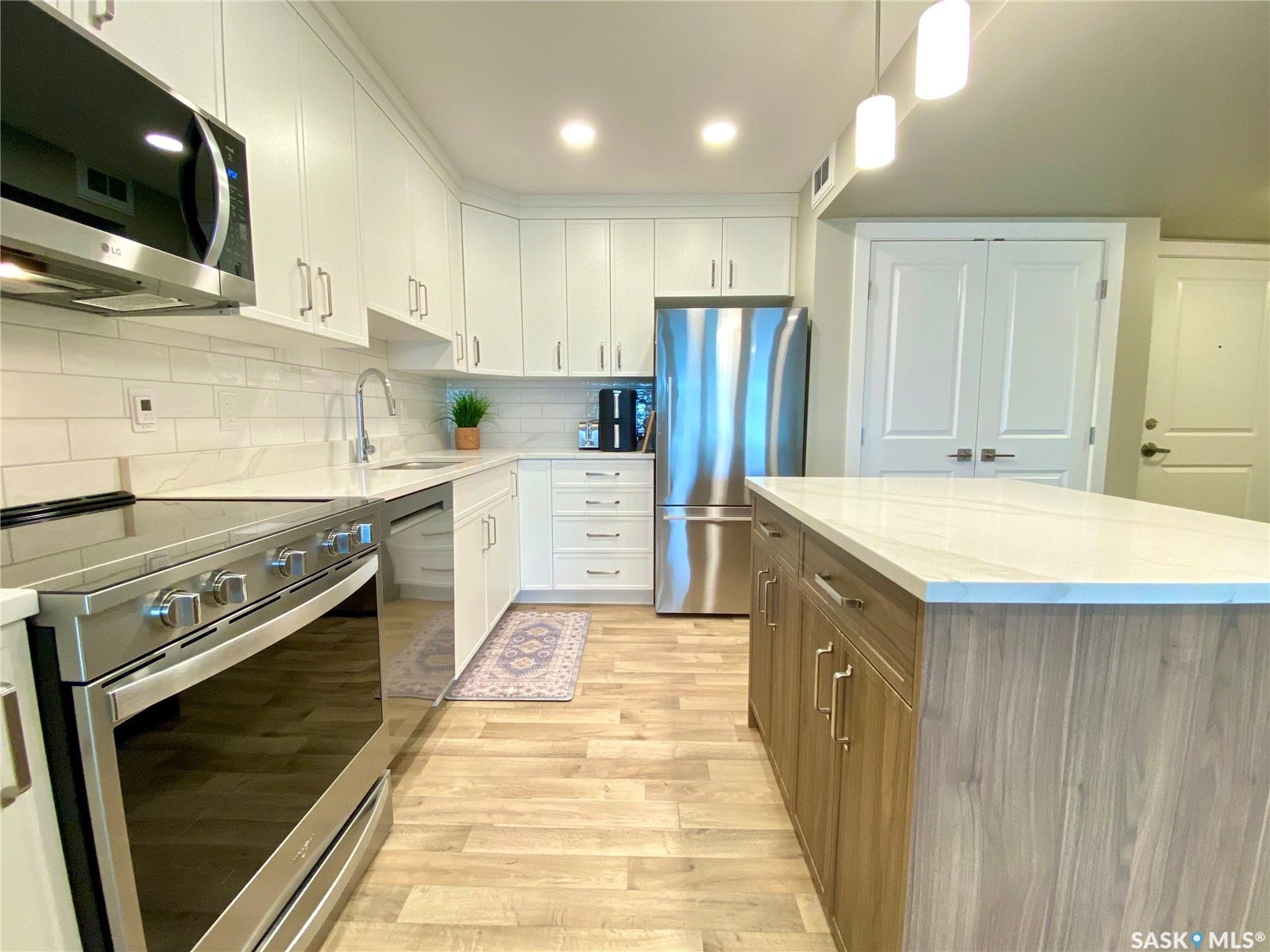 Modern kitchen featuring white cabinetry, stainless steel appliances, a wood-finish island with a light-toned countertop, and wood-finish flooring
