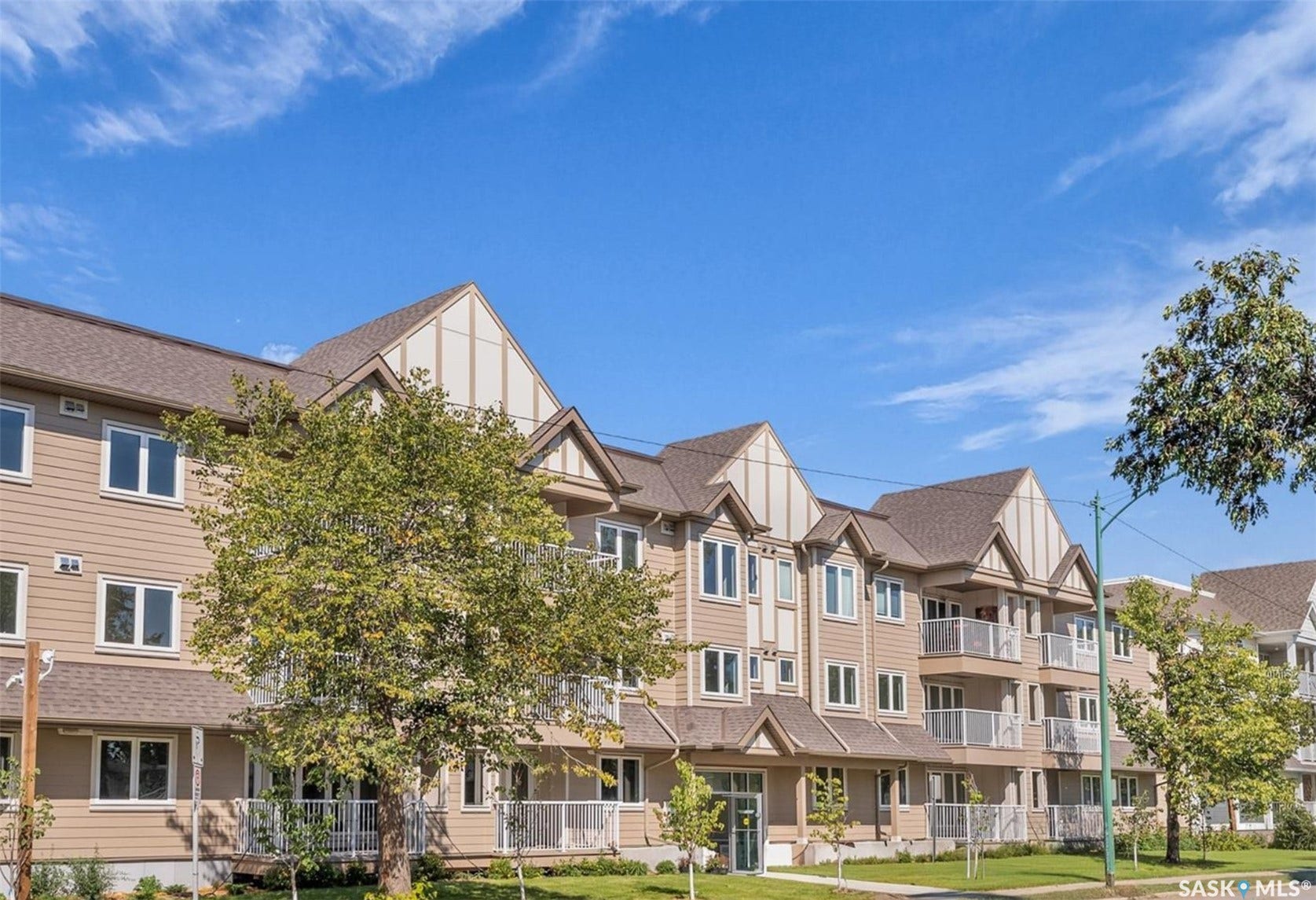 Multi-level residential building featuring dormer windows, individual balconies with white railings, and a neatly maintained lawn