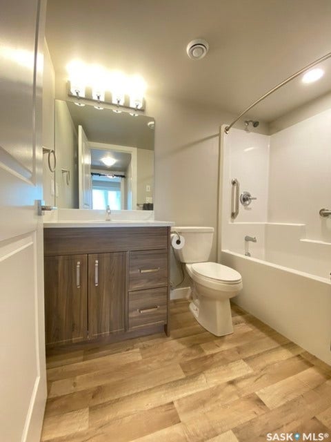 Wood-finish plank flooring, vanity with wood-finish cabinetry, white countertop, and rectangular mirror