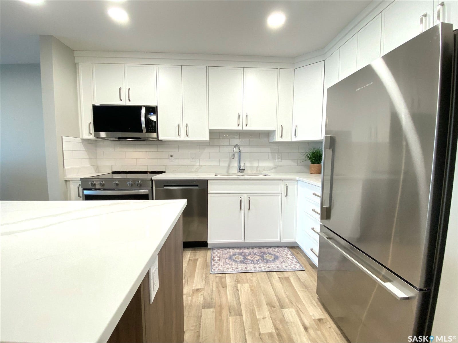 White cabinetry with brushed nickel hardware, stainless steel appliances, white subway tile backsplash, light-colored wood-finish flooring, and white countertops