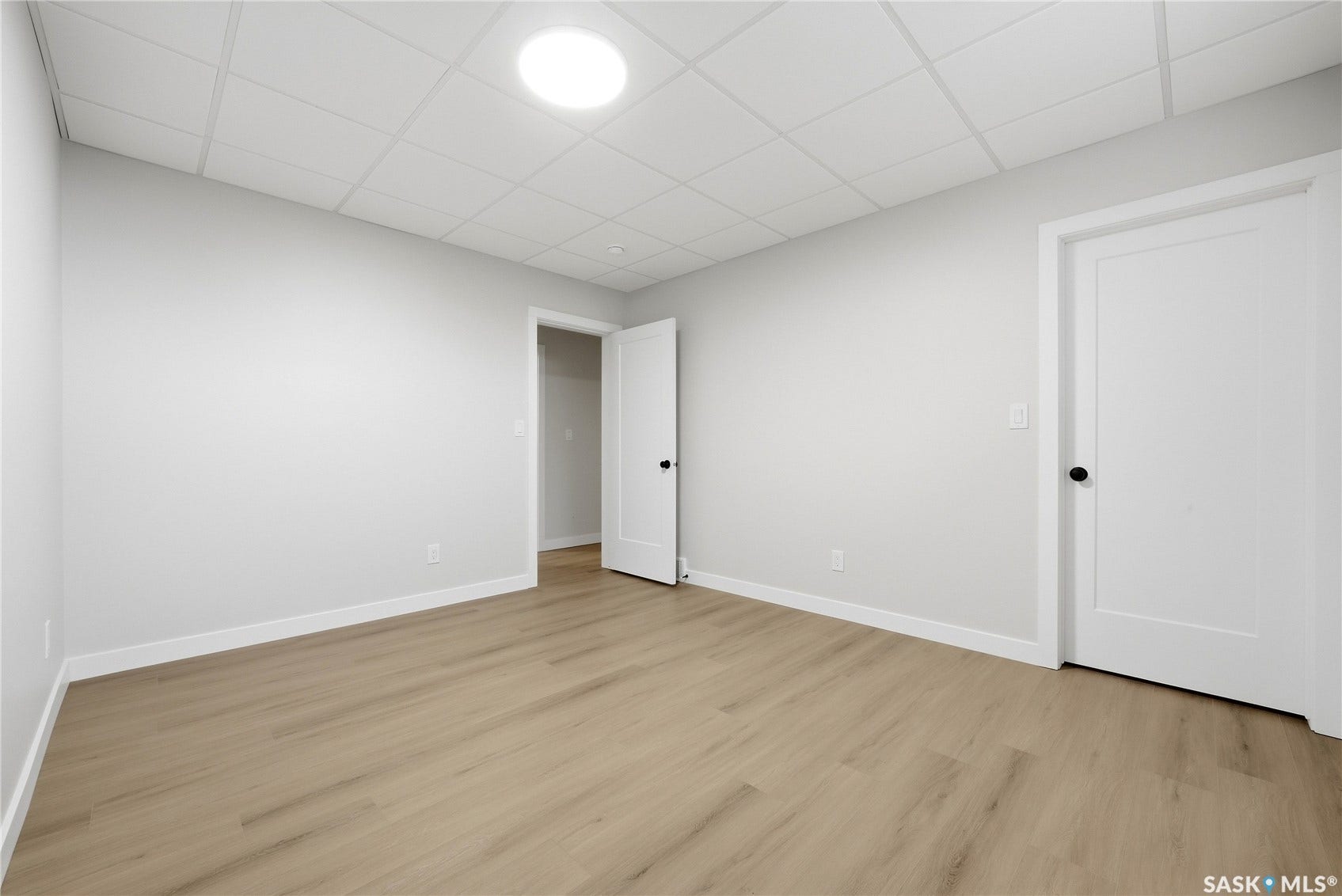Wood-finish flooring, white walls, and a suspended ceiling with an integrated circular light fixture