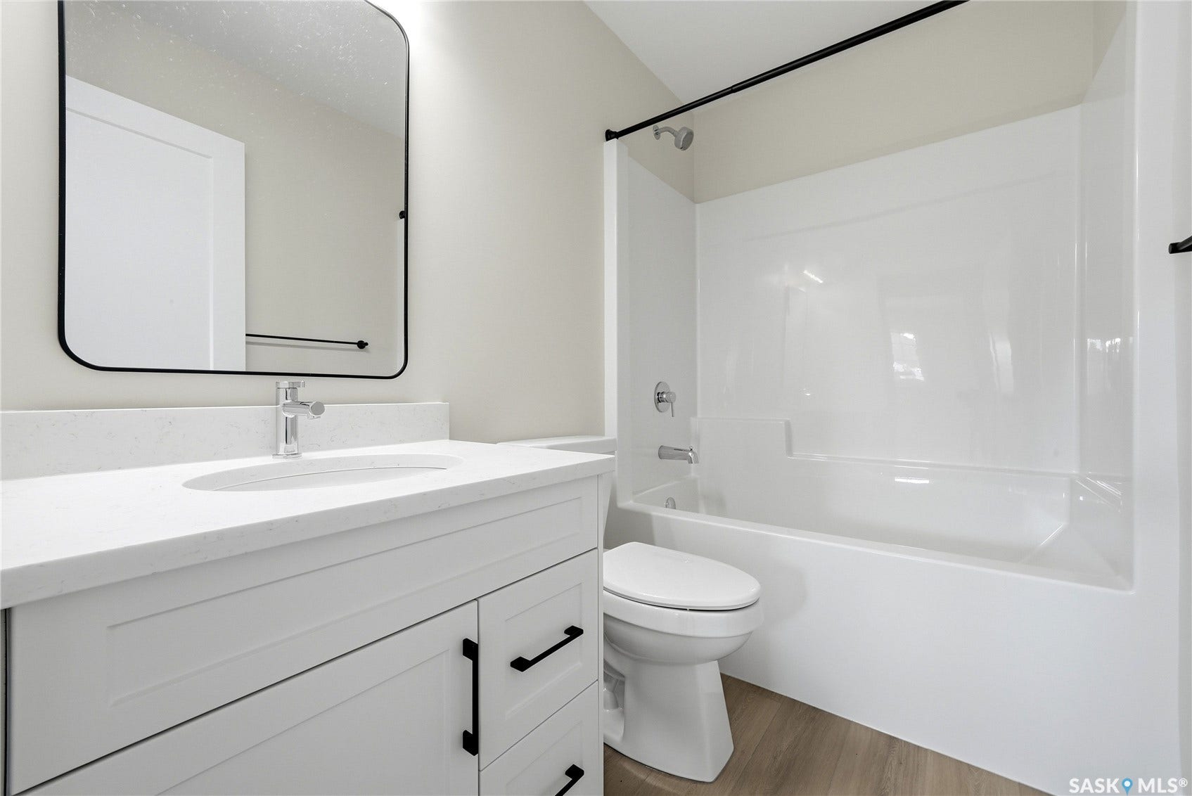 White shaker-style vanity with dark hardware, a rectangular undermount sink, and a light-toned countertop