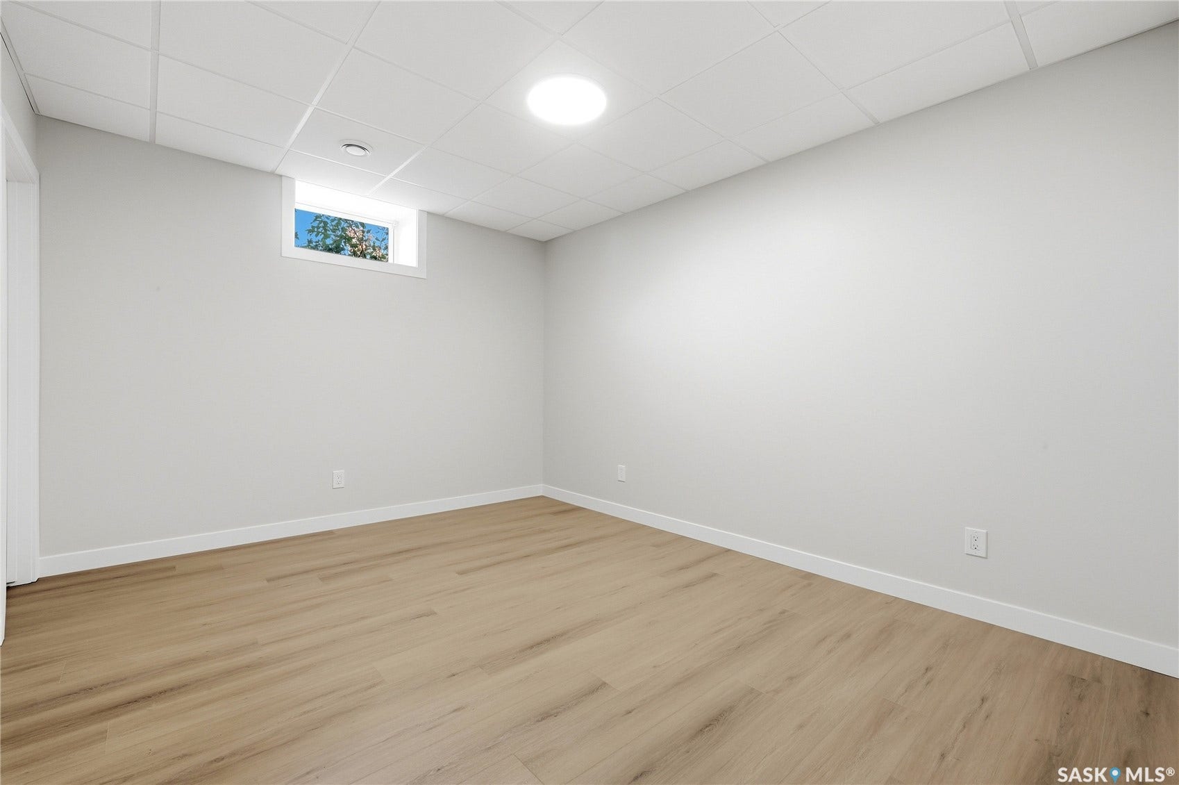 Light wood-finish flooring, white walls, drop ceiling with integrated lighting, and a horizontal window