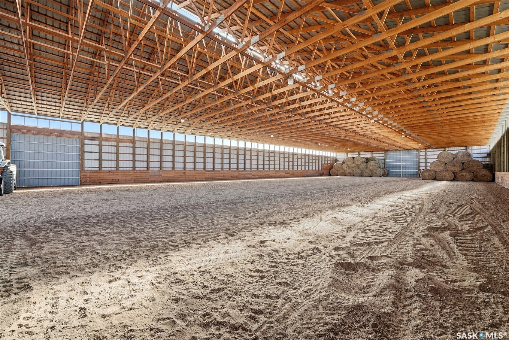 Spacious indoor arena featuring a high exposed timber beam ceiling, extensive natural light panels, and a large roll-up door