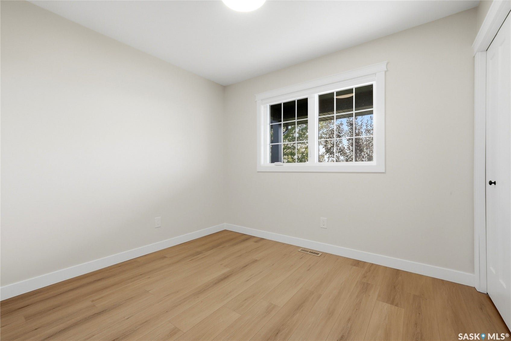 Wood-finish flooring with white trim, a double-pane window, and a flush-mount ceiling light