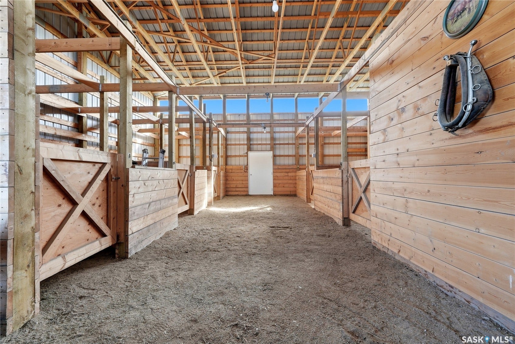 Spacious barn interior with multiple stalls featuring horizontal wood paneling and cross-brace details