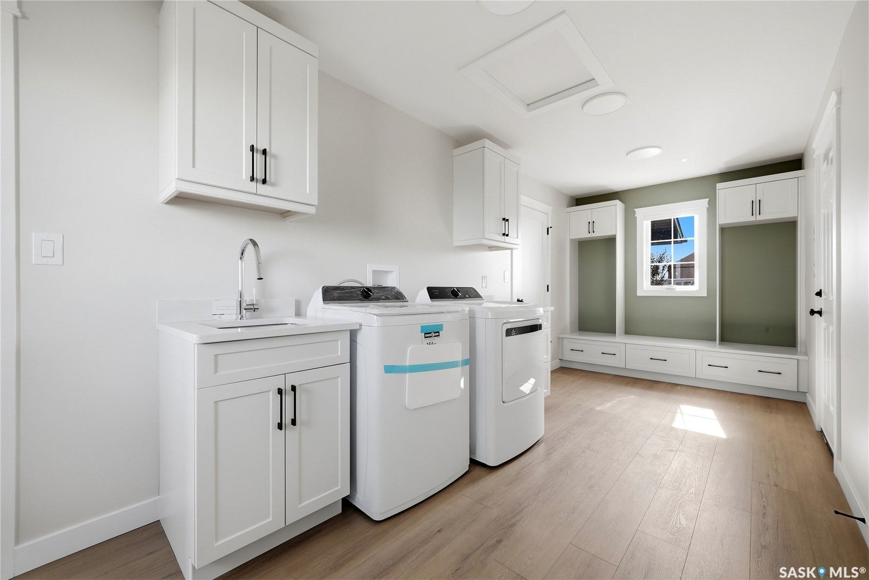 White cabinetry, wood-finish flooring, built-in mudroom storage, utility sink, and a single window