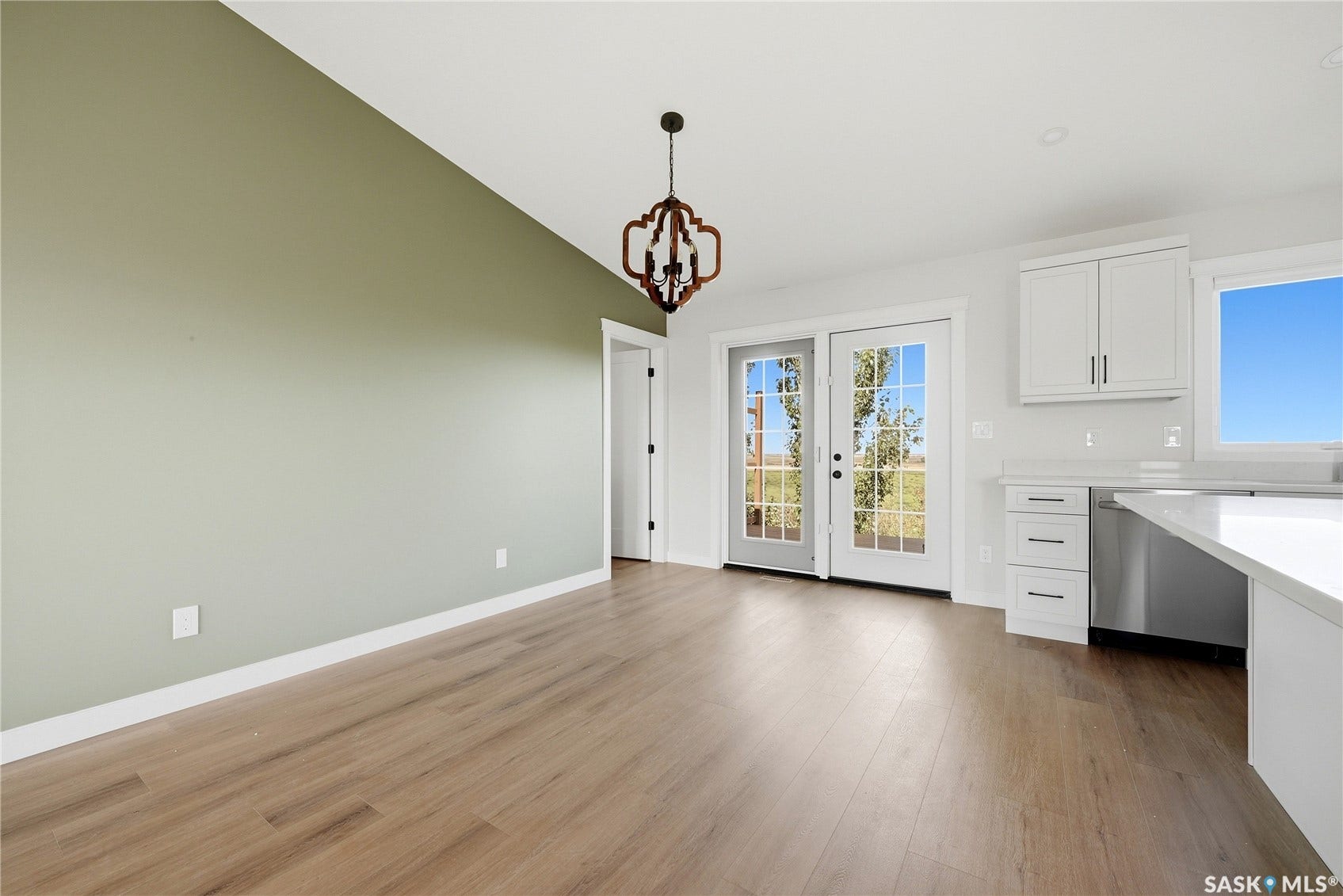 Vaulted ceiling with a decorative chandelier, dual pane French doors, wood-finish flooring, white cabinetry with hardware, and a built-in dishwasher