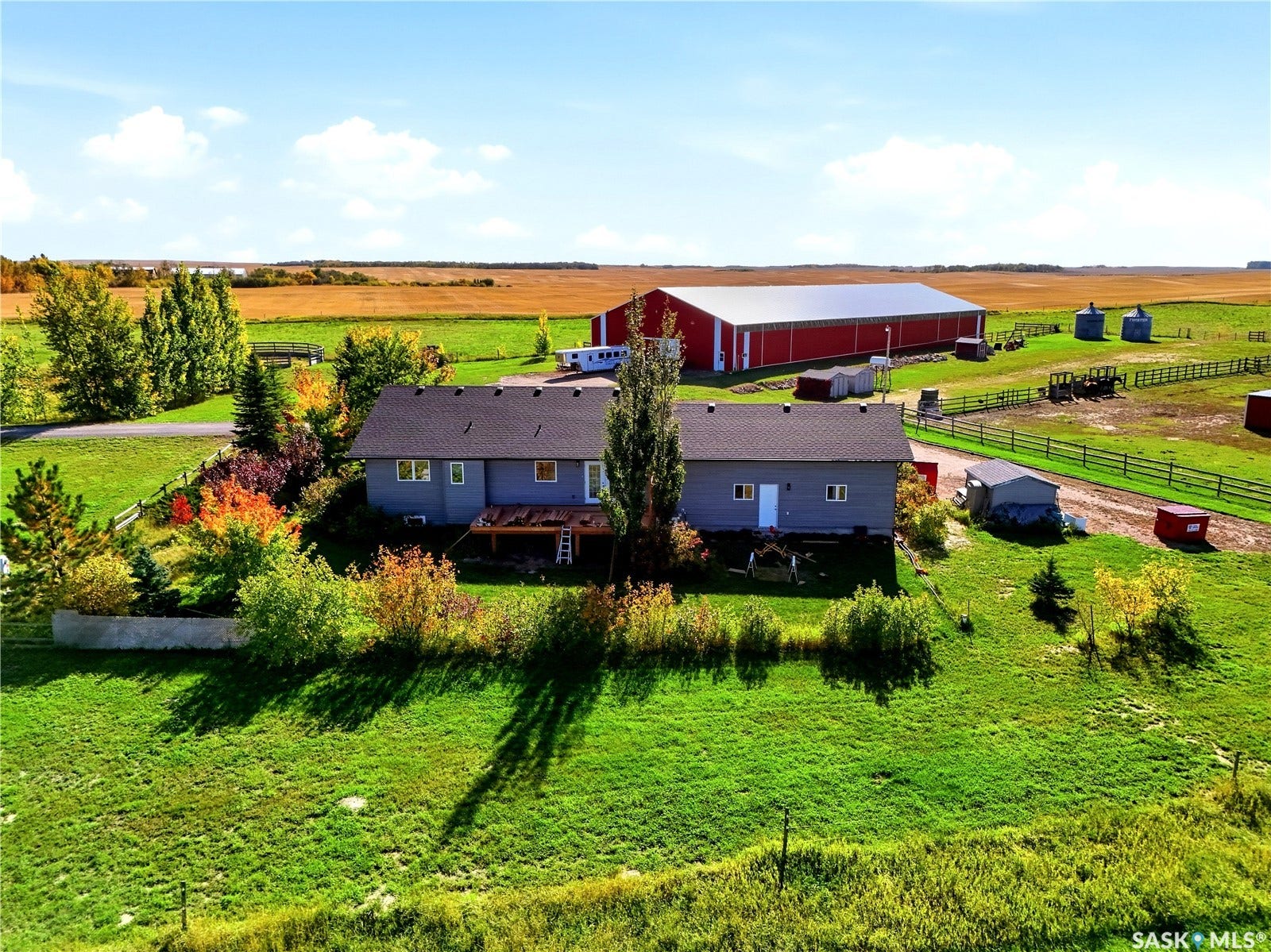 Spacious property featuring a primary residence with light gray siding, an expansive red barn, multiple outbuildings, and a large green lawn