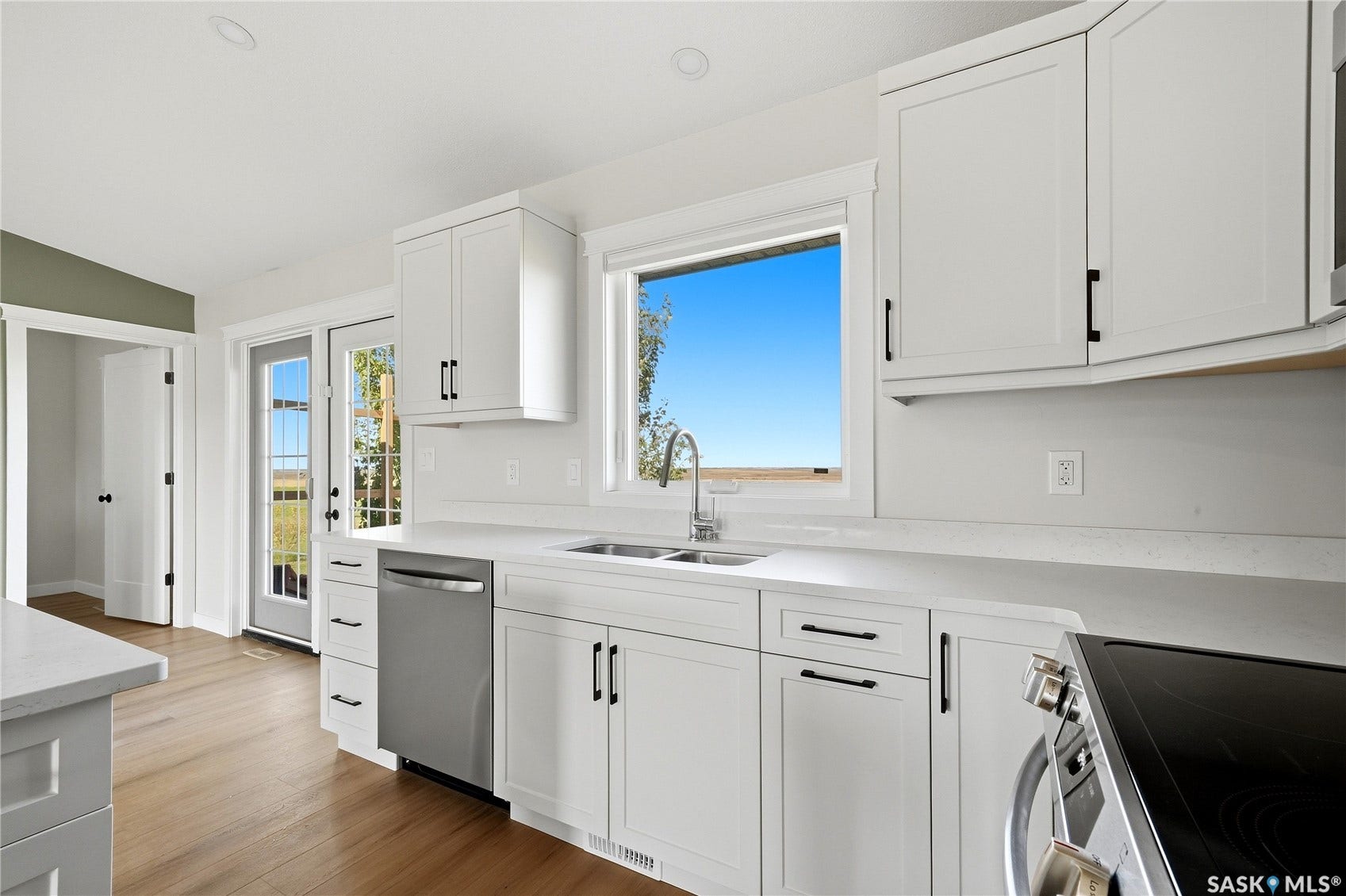 White shaker cabinetry with black hardware, stainless steel dishwasher, wood-finish flooring, white countertops, and a window above the sink