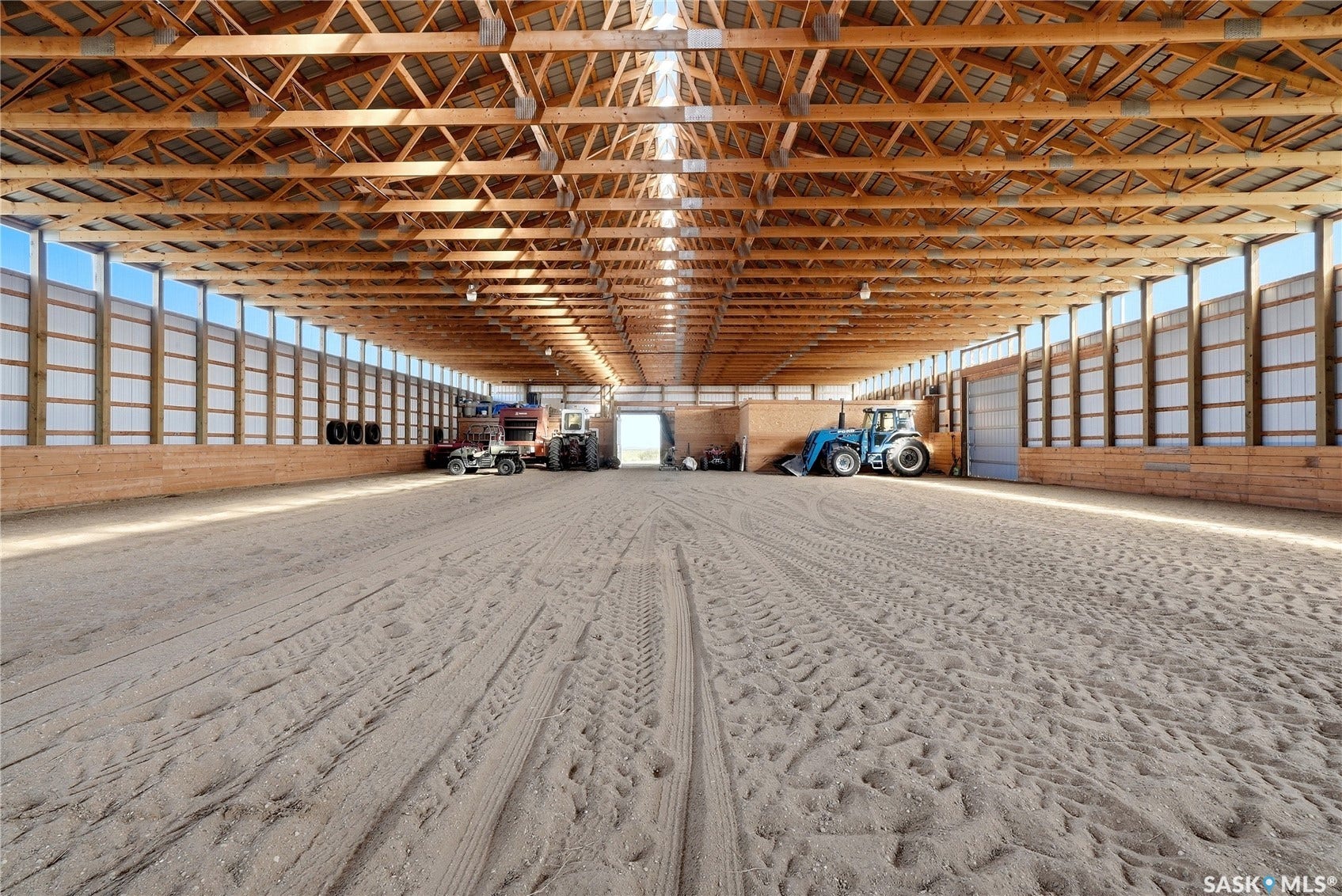 Expansive indoor arena with a sand footing, exposed wood beam ceiling, and translucent wall panels providing natural light