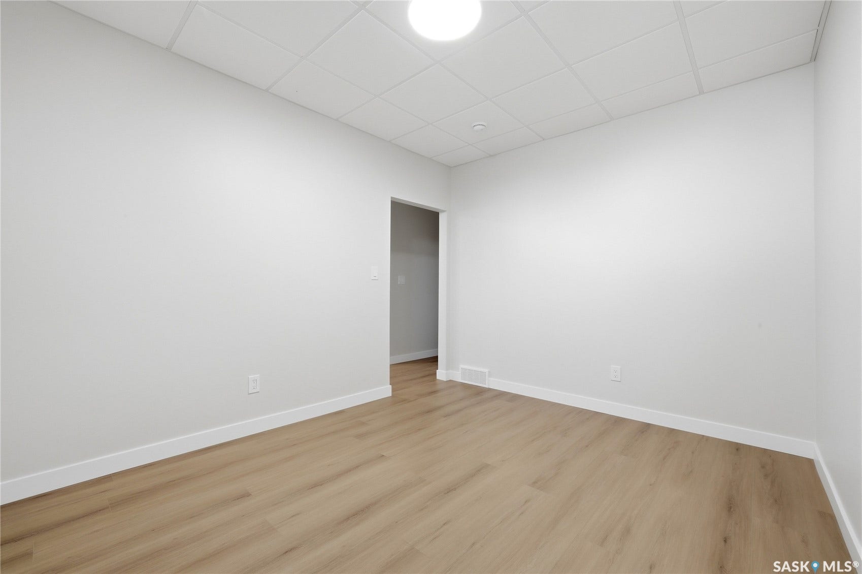 Wood-finish flooring, white walls, drop ceiling with integrated lighting, white baseboards, and a doorway