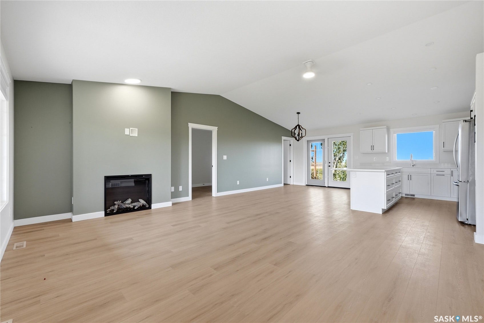 Spacious interior with wood-finish flooring, an electric fireplace, vaulted ceilings, white cabinetry, and stainless steel appliances